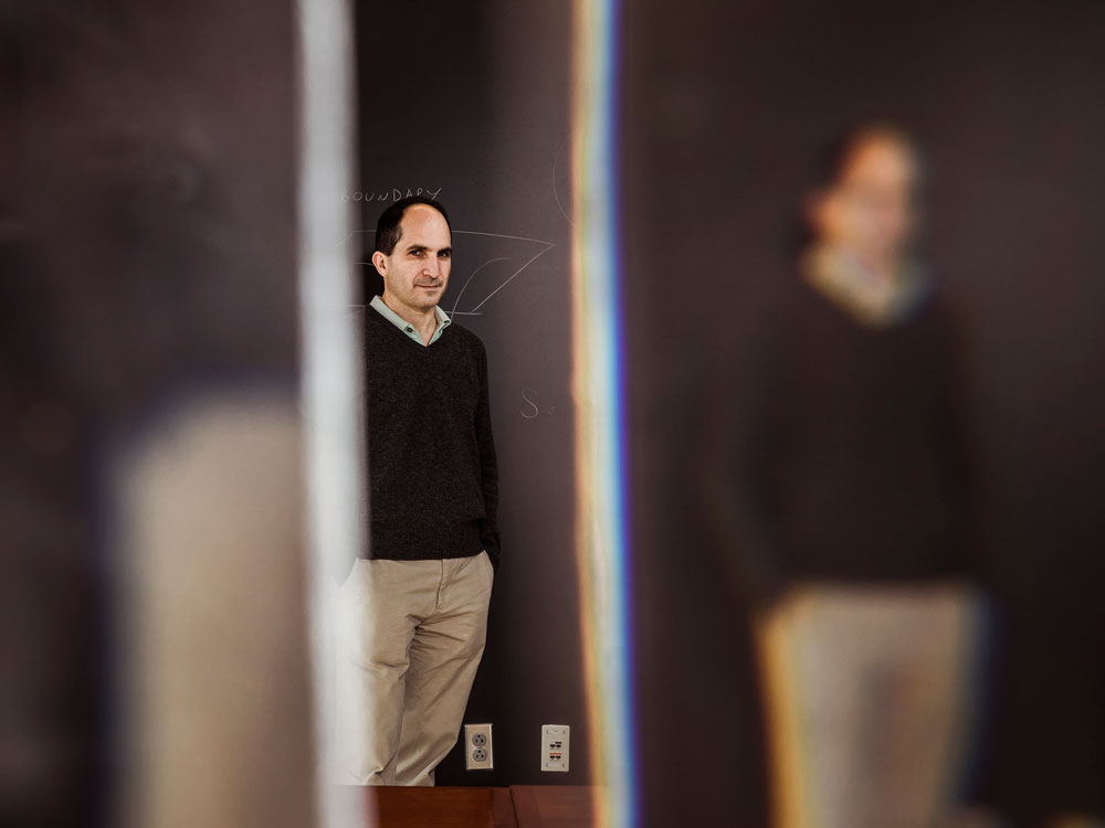 Juan Maldecena standing off-center in front of a blackboard with blurry reflections on either side