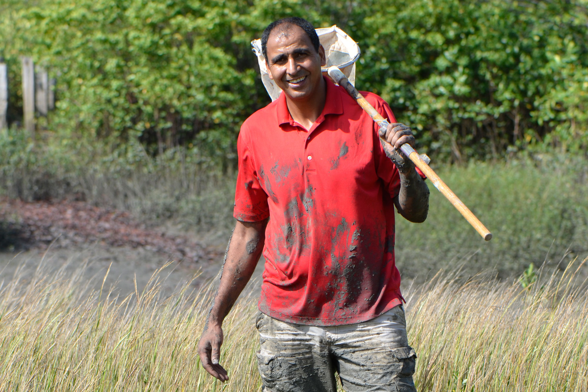 Abderrahman Khila covered in mud, carrying a bug net and wearing a red shirt