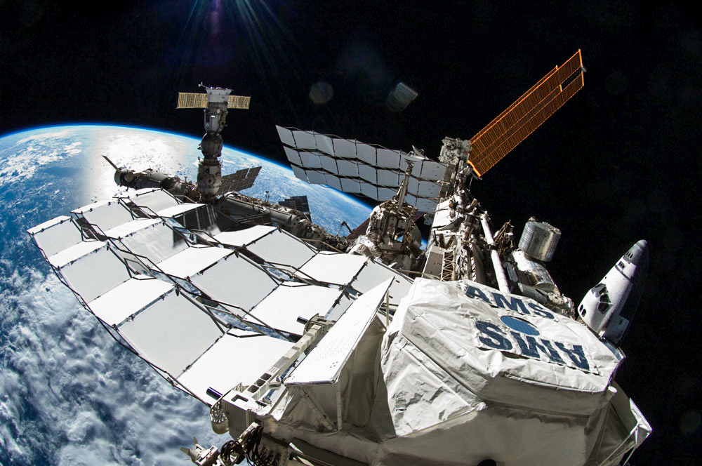 The Alpha Magnetic Spectrometer, seen here in the foreground of the International Space Station, could eventually settle the dark matter-vs.-pulsars debate.