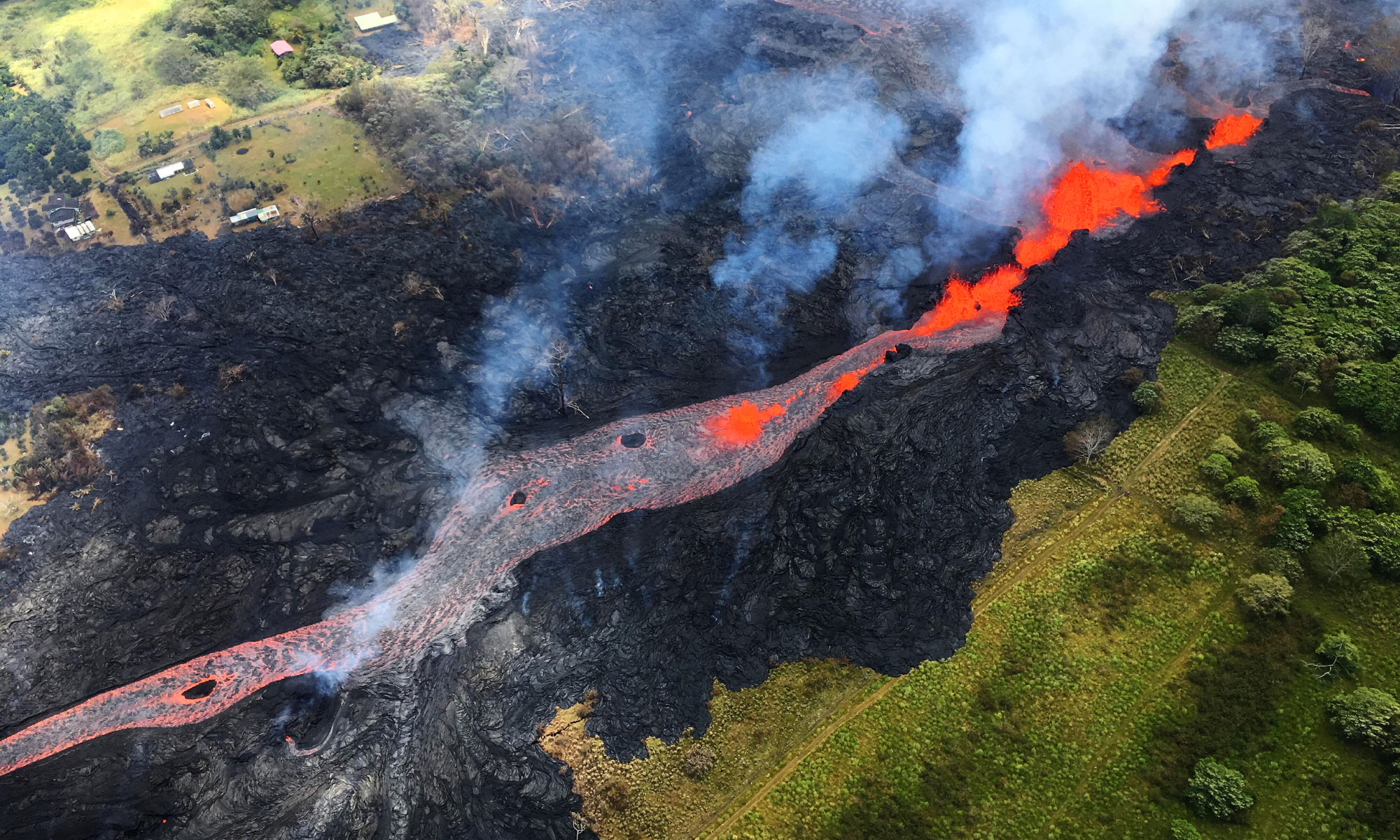 Aerial photo showing a river of lava flowing through the land.