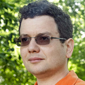 Mark Braverman, in an orange shirt, stands on a path lined with trees.