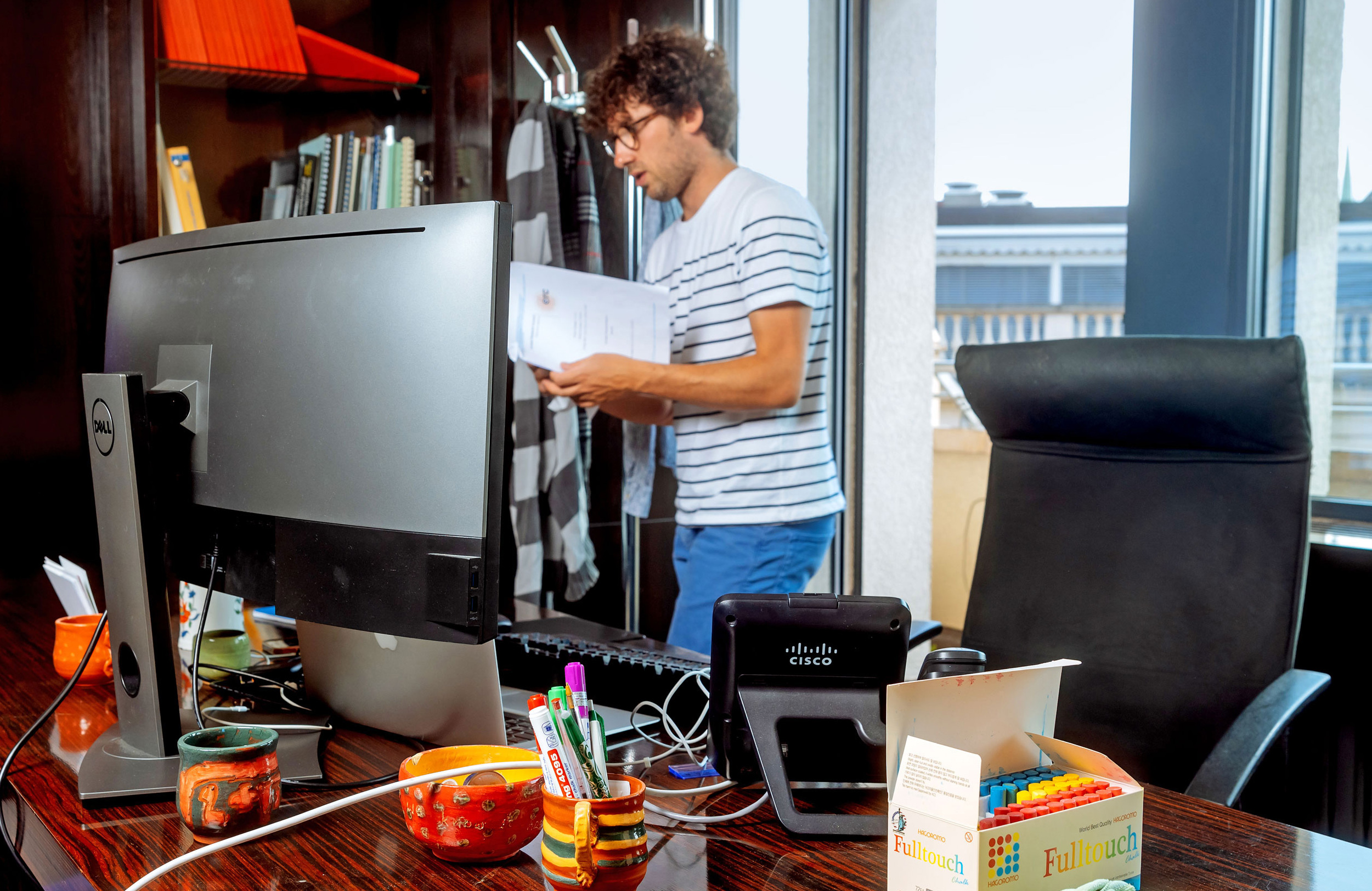 large photo of a man with dark curly hair standing behind a desk with a large computer