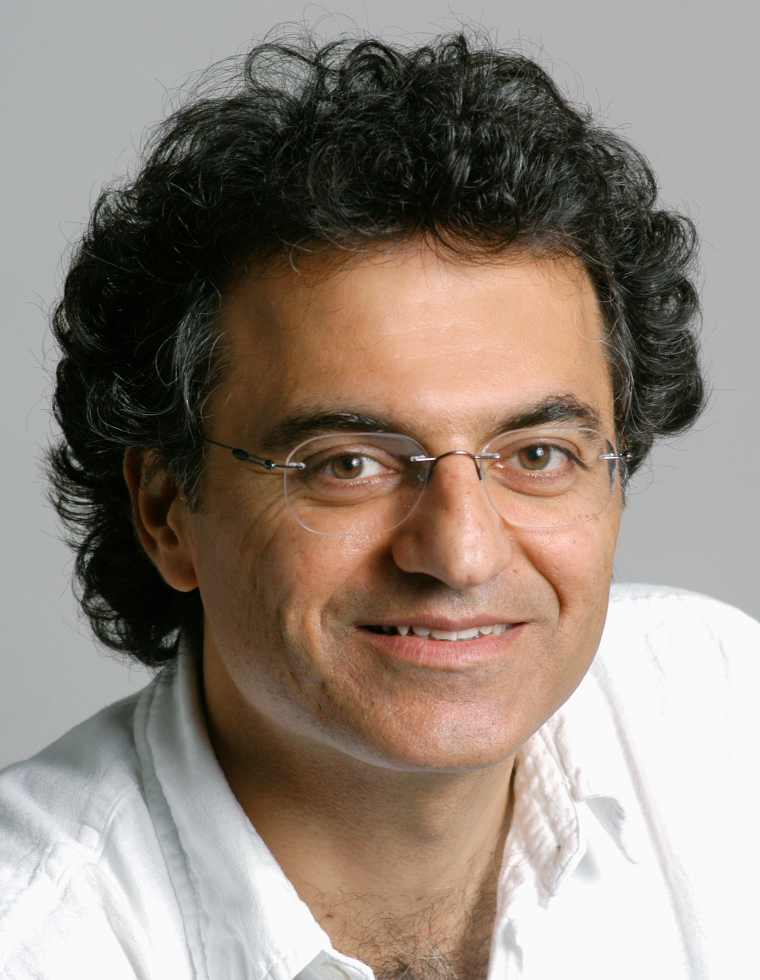 Photo of a man wearing thin wireframe glasses, a white shirt, short black curly hair, smiling and looking into the camera.