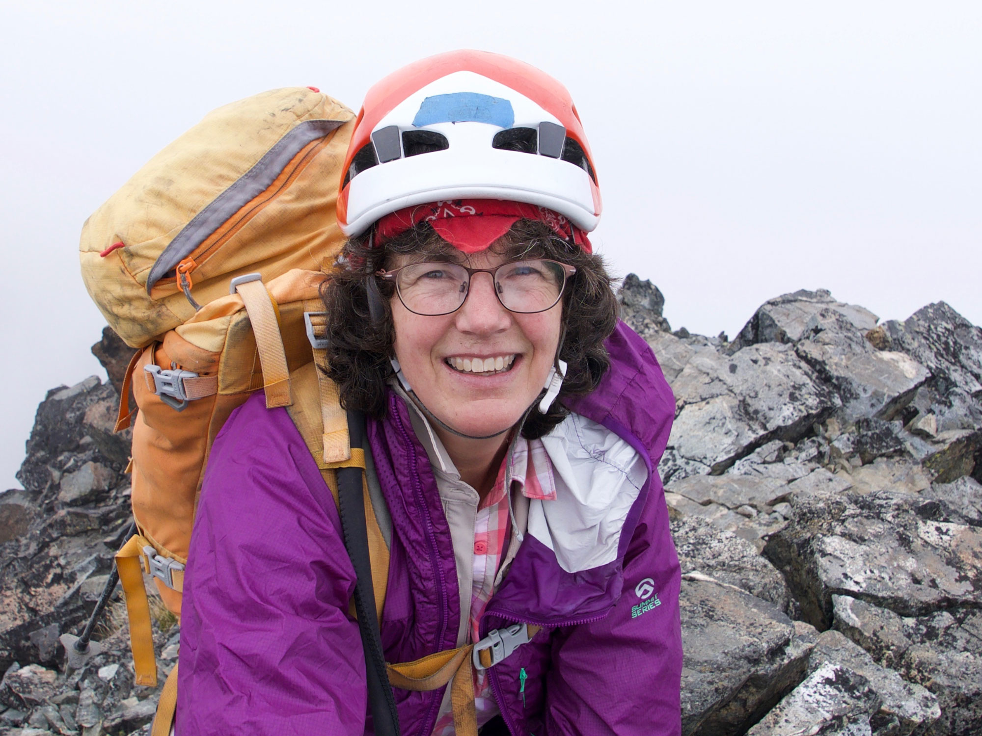 Nelson, wearing hiking gear, smiles at the camera at the top of a rocky outcrop.