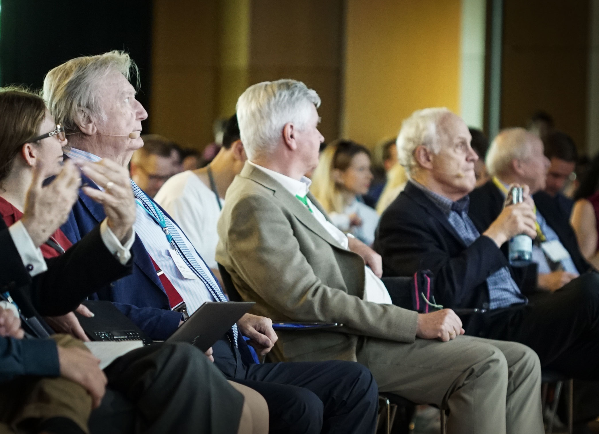 Carlo Rubbia seen in profile, sitting in a crowd of physicists all looking to the right.