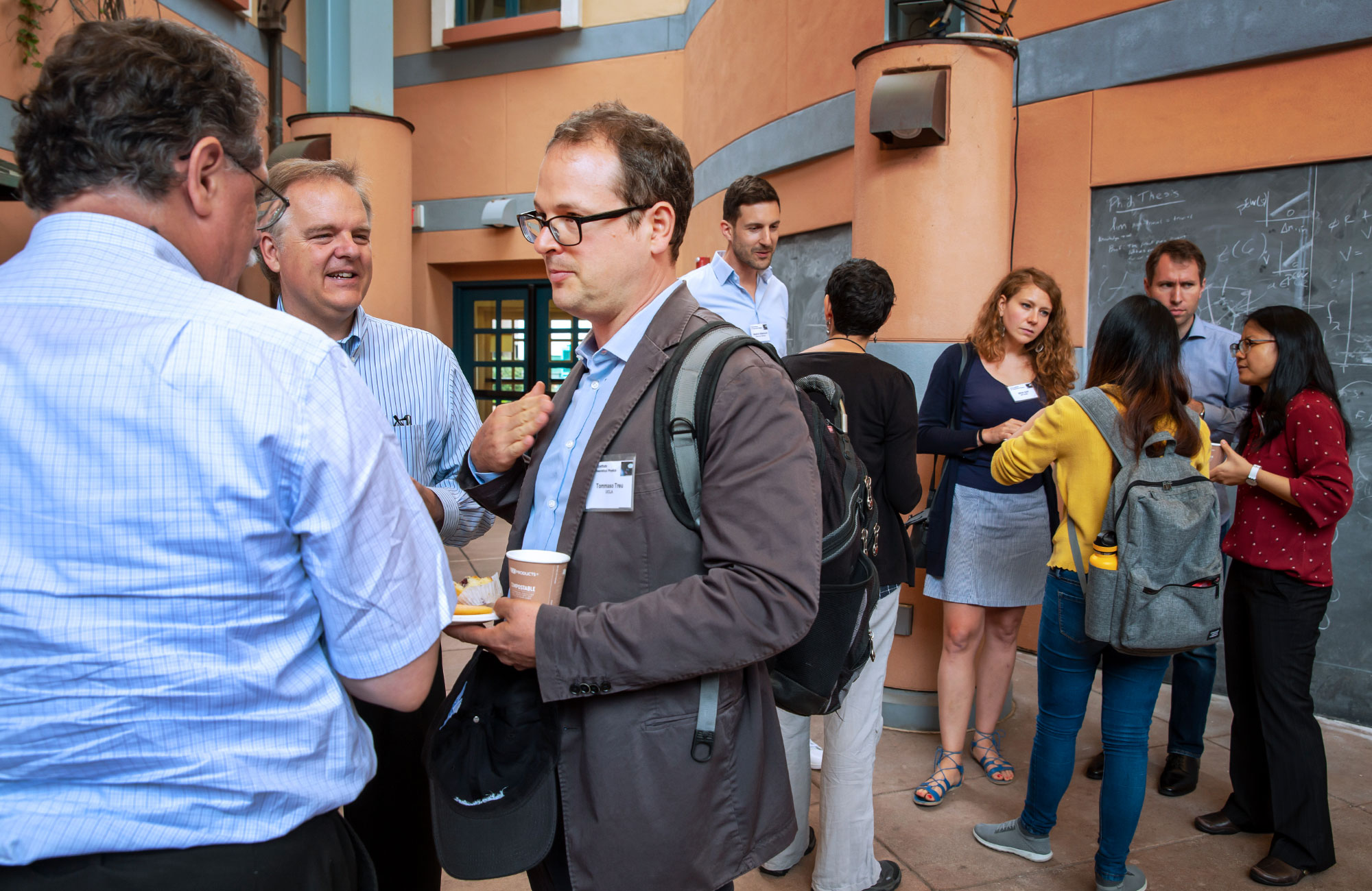 Tomasso Treu holding a cup of coffee and chatting with fellow cosmologists in a courtyard at the Kavli Institute for Theoretical Physics.