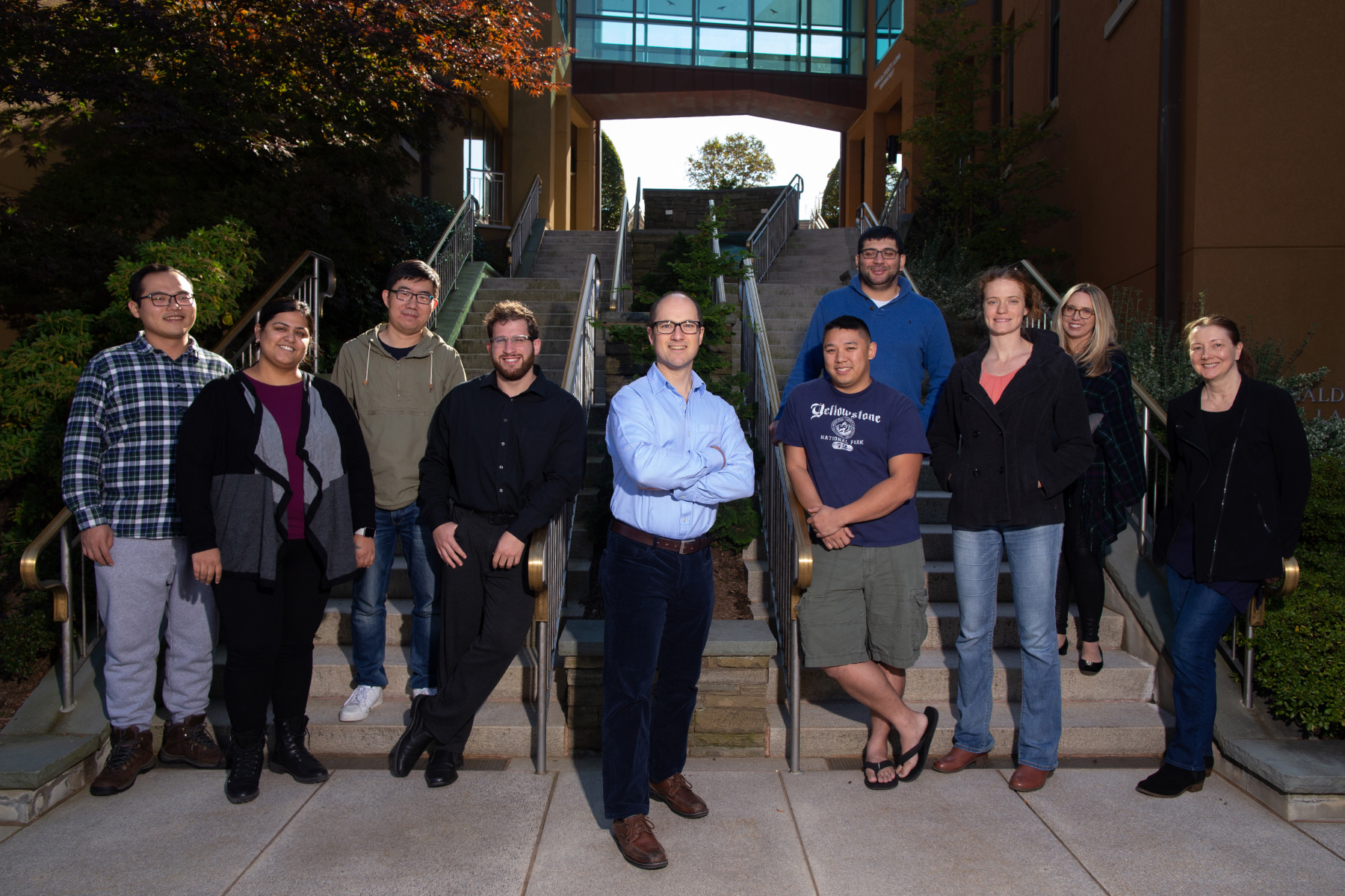 Adam Siepel and nine members of his laboratory pose in front of steps on the Cold Spring Harbor Laboratory campus.