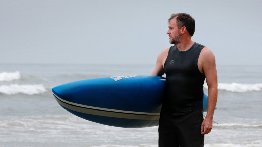 Craig Callender holding a paddleboard at the beach.