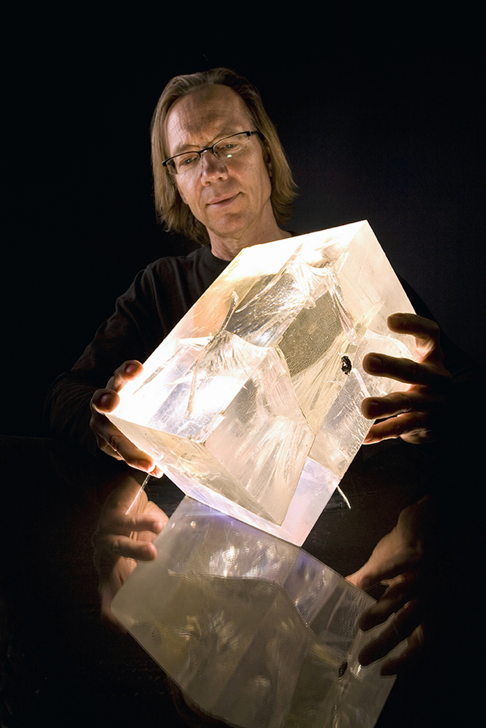 Portrait of Paul Johnson against a black background, holding an illuminated block of plastic.