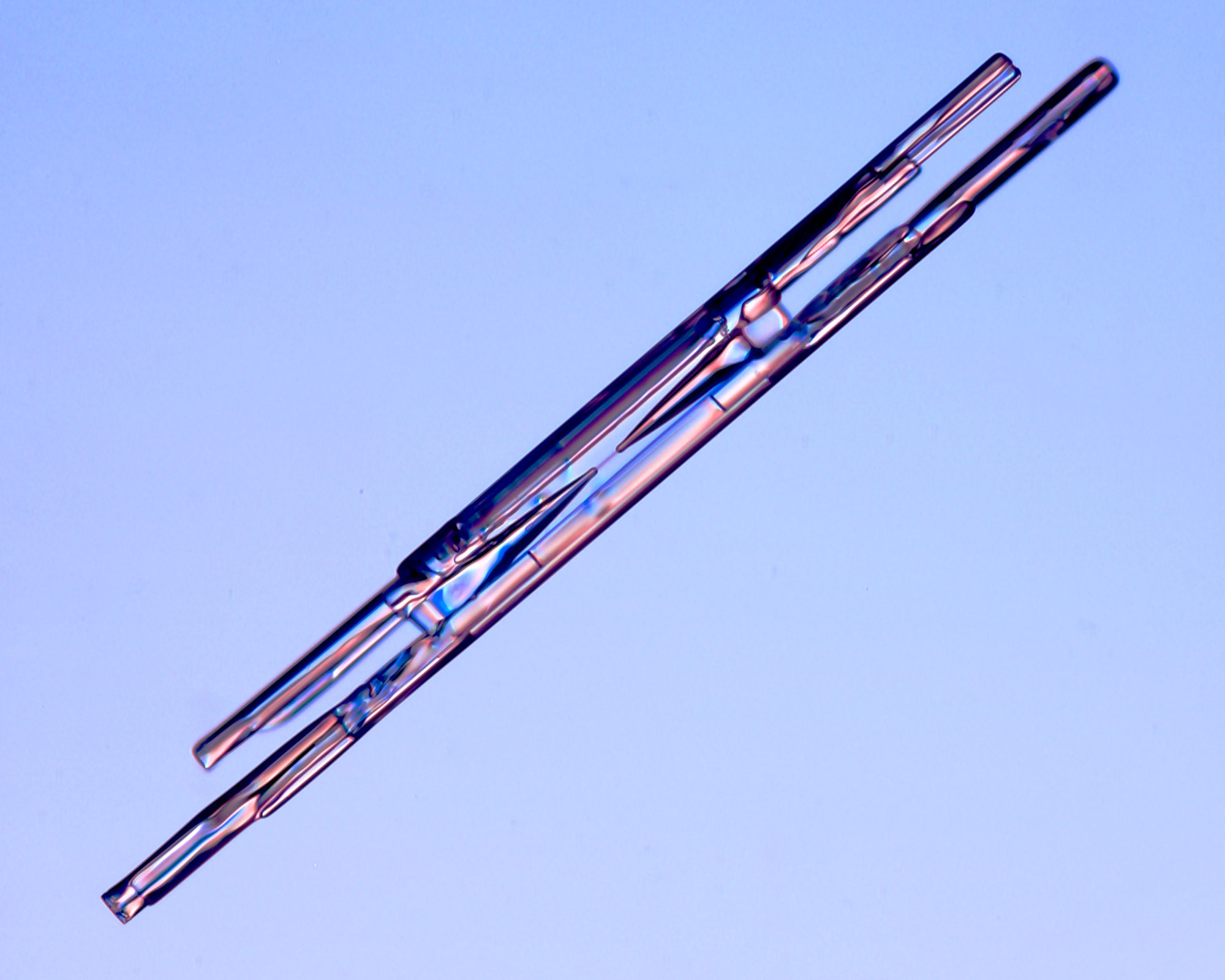 One of three close-up images of column-like snowflakes on a blue background.