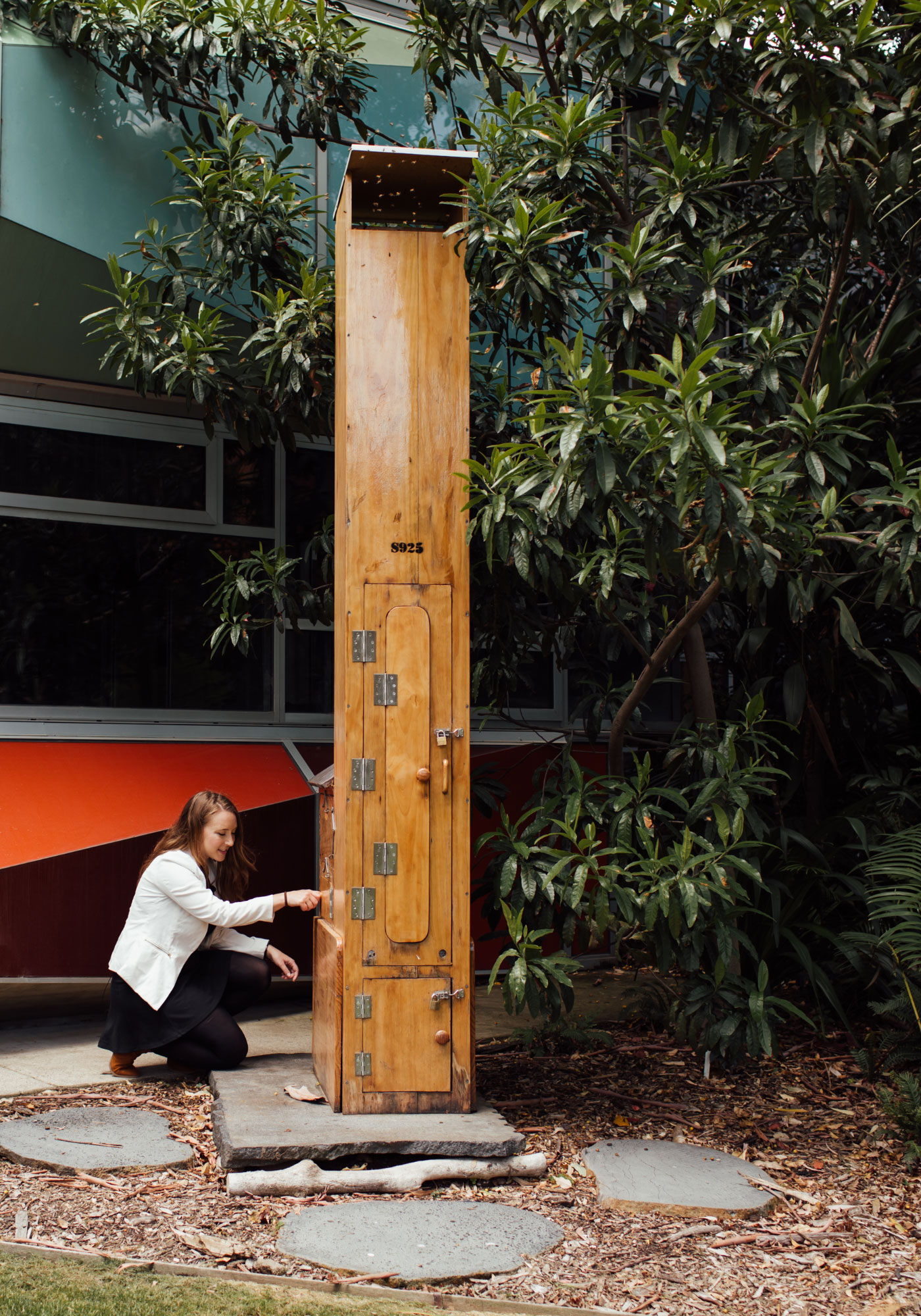 One of two grouped photos: This one shows Scarlett Howard kneeling at a chimney hive housing honeybees.