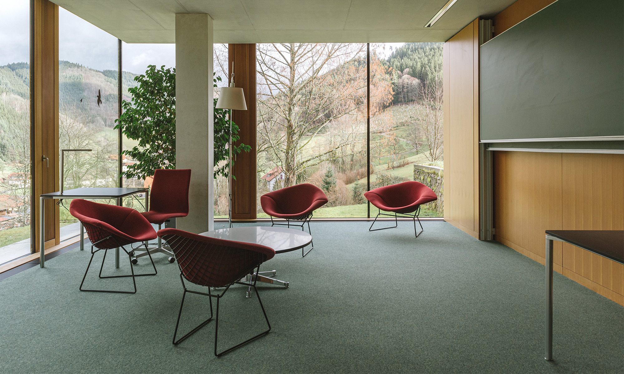 Photo of chairs, tables and a chalkboard at Oberwolfach, in front of a wide window revealing forests outside