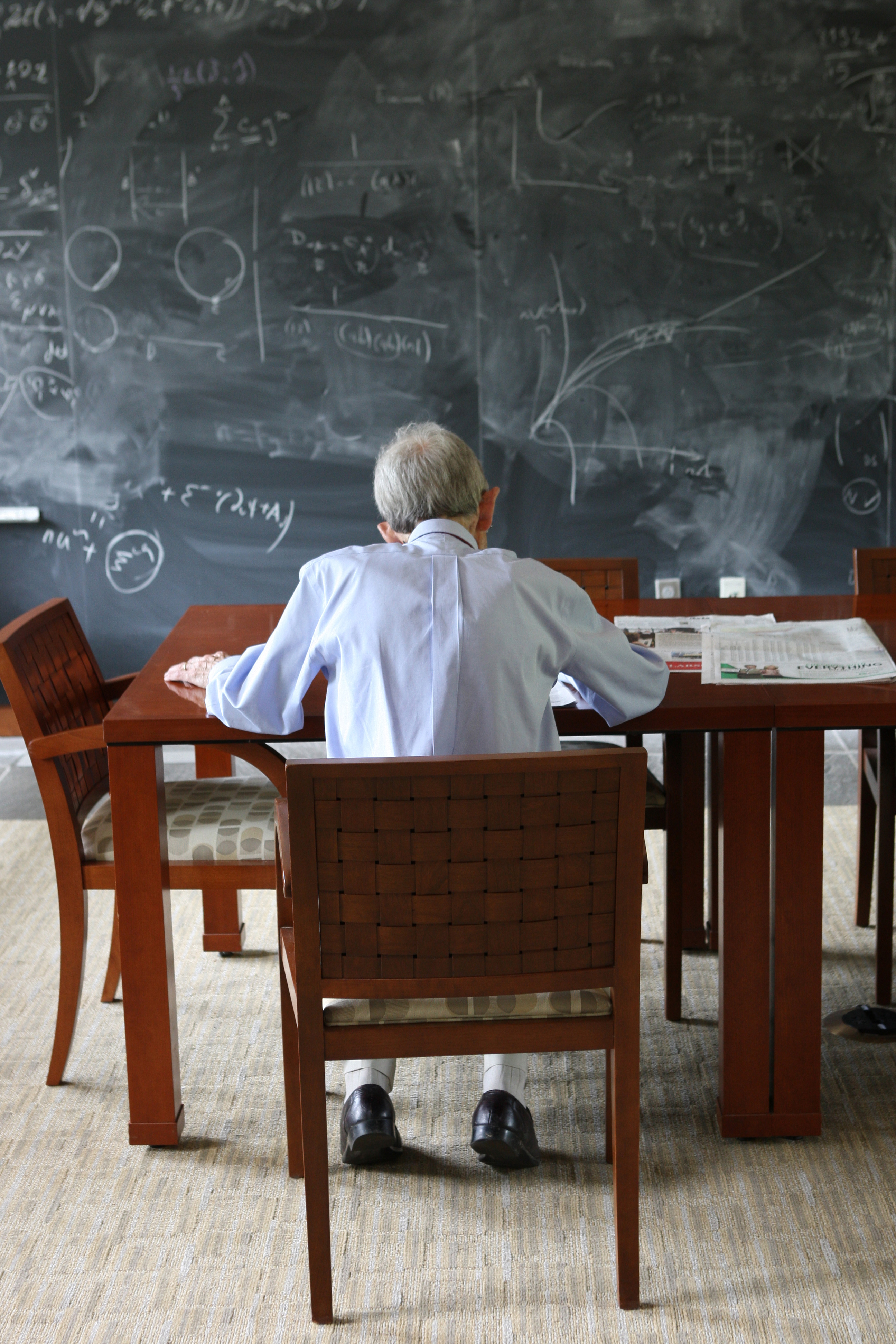 Photo of Freeman Dyson sitting at a table in front of a chalkboard