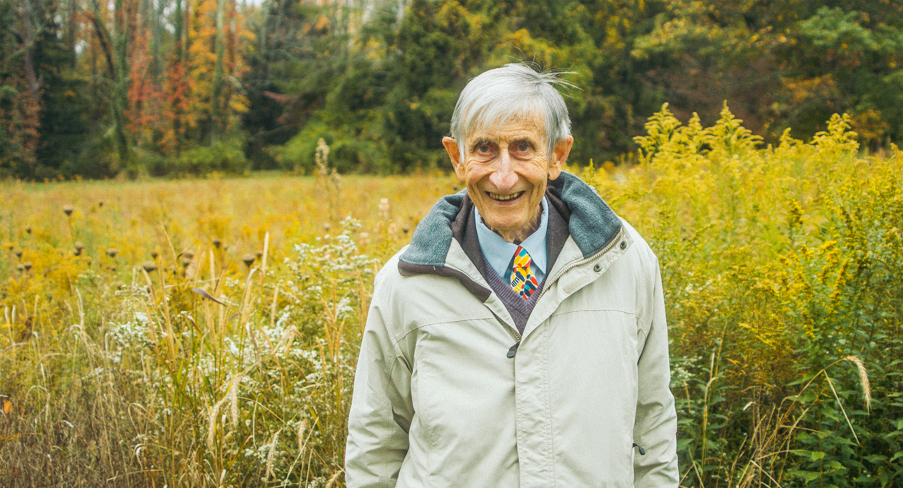 Photo of Freeman Dyson standing in a meadow in front of a forest