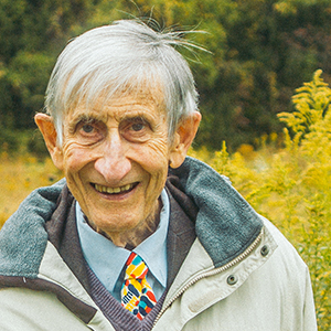 Photo of Freeman Dyson standing in a meadow in front of a forest