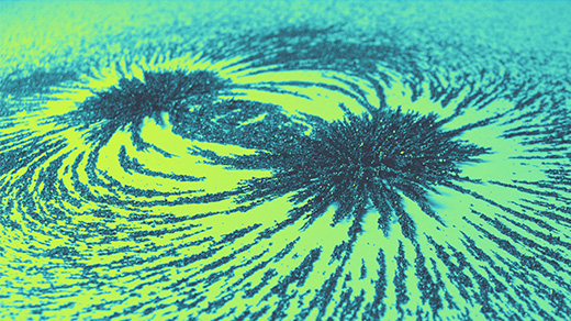 Photo of iron filings spread along magnetic field lines on a green and yellow background