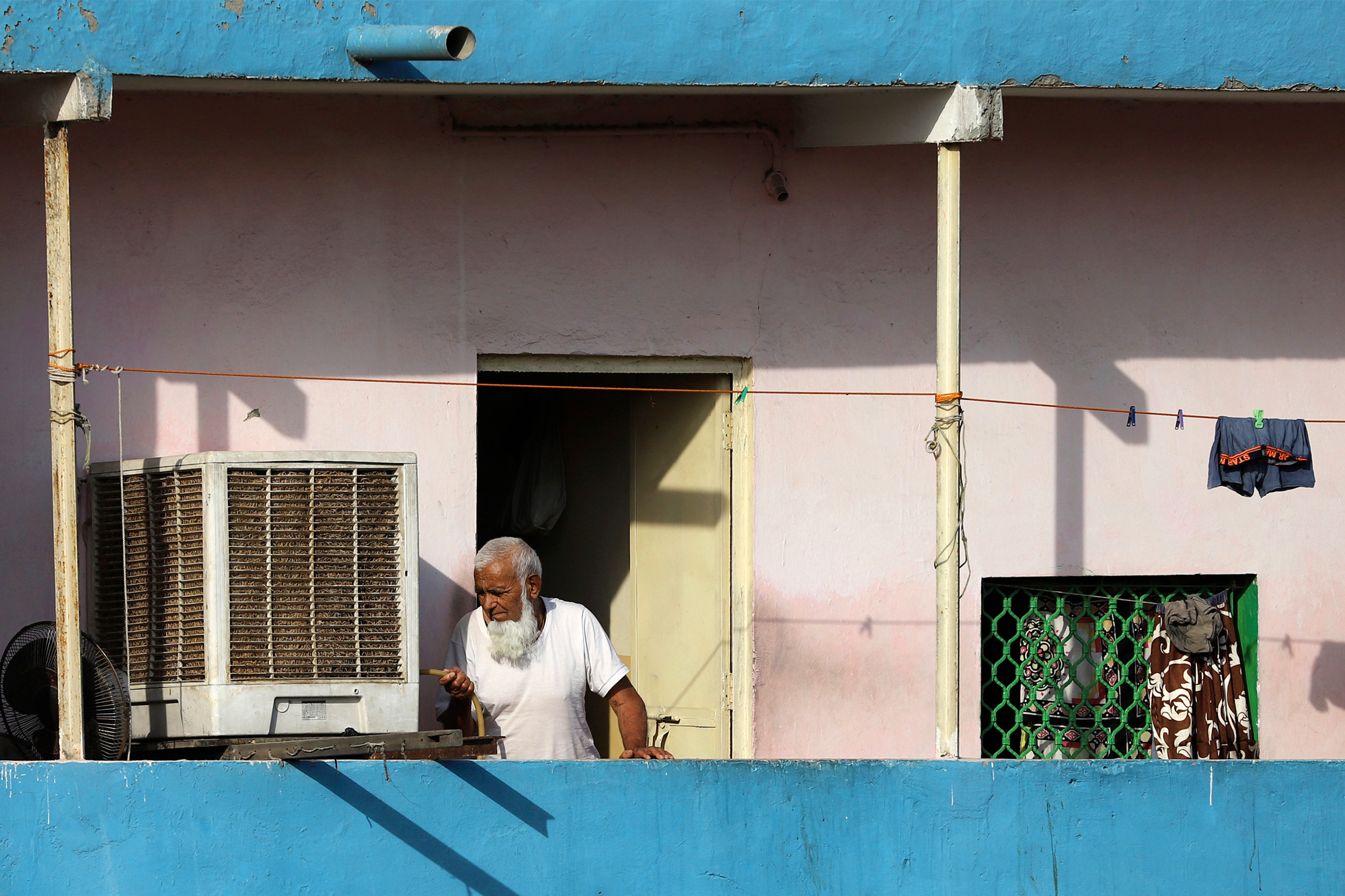 Older man on a balcony pours himself water in Delhi.