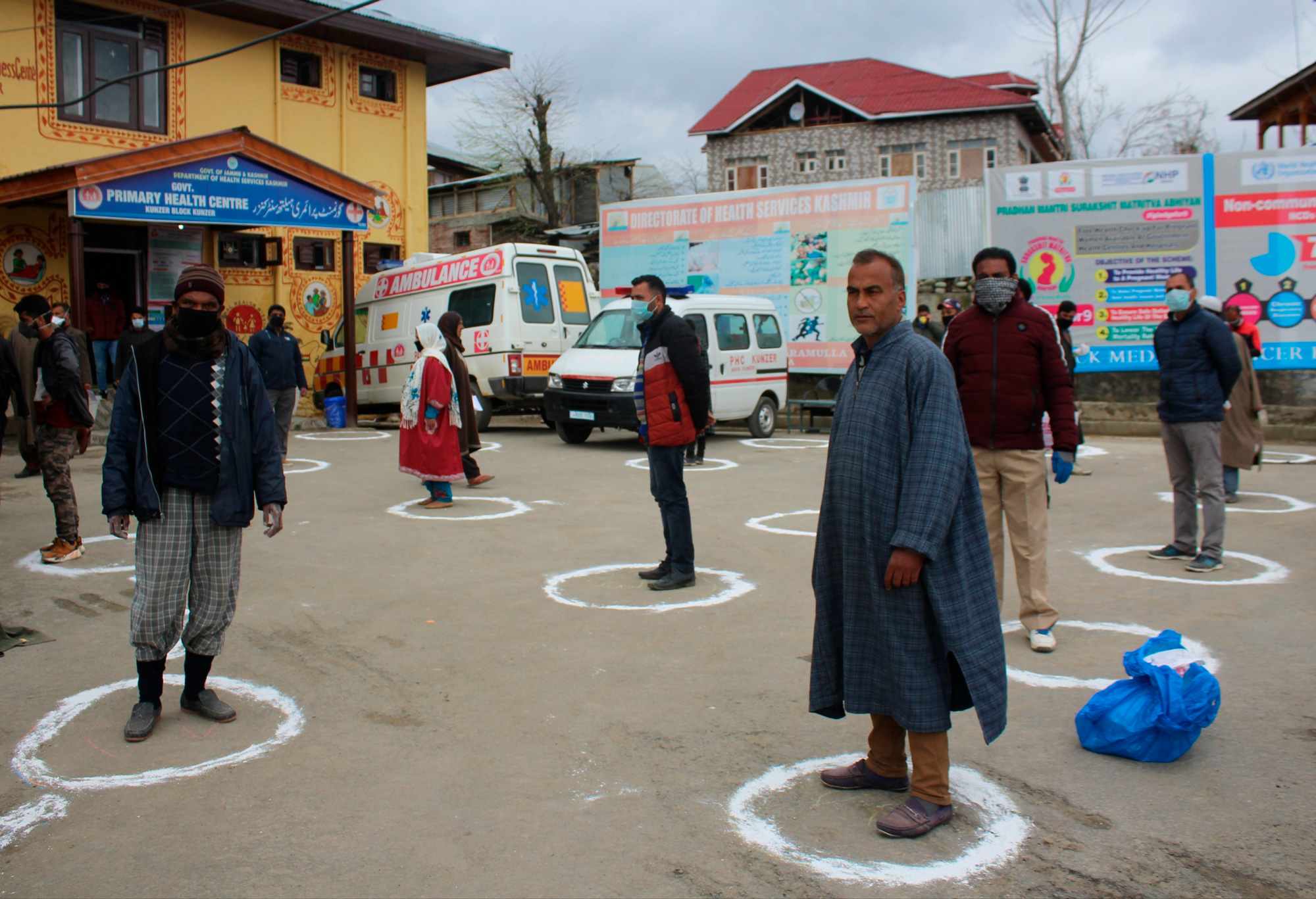 In the street outside a hospital in Srinigar, people wait in small circles marked on the street to stay separated.