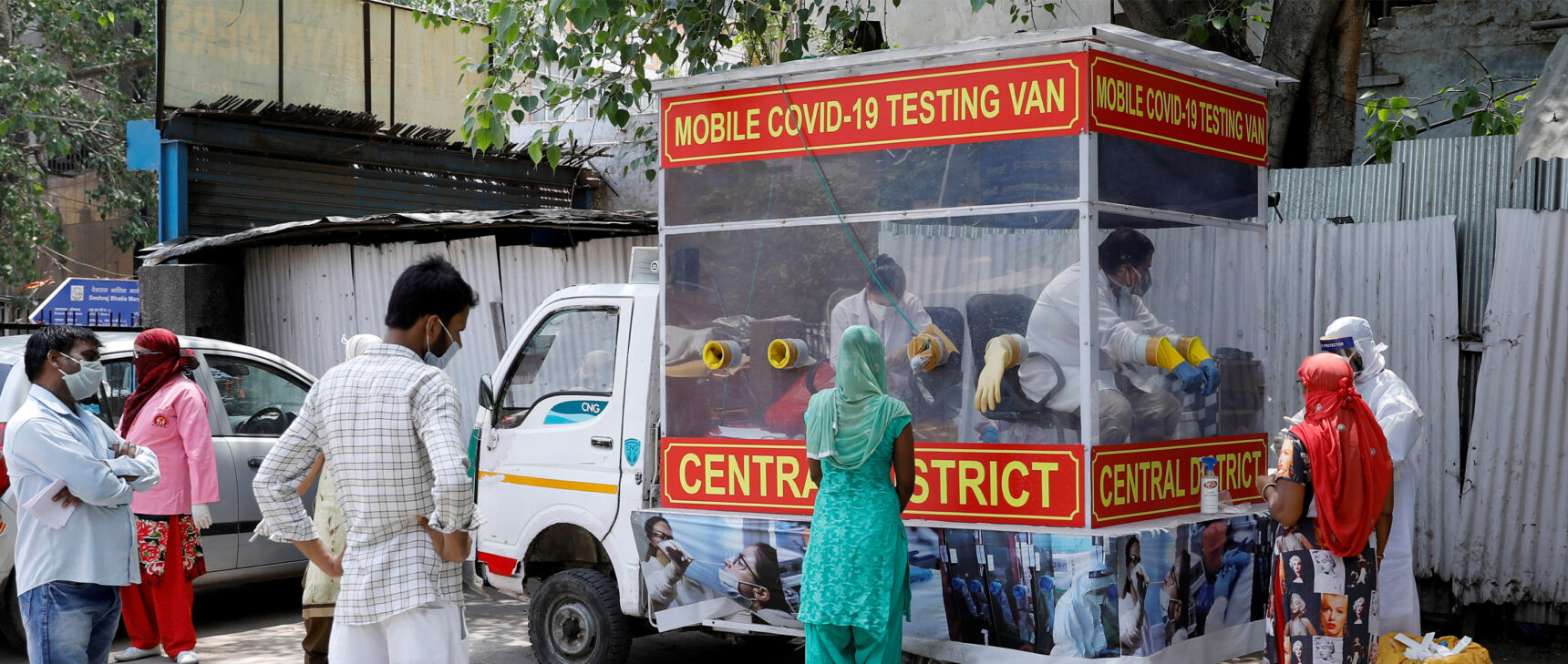 People in India stand near a red van that serves as a mobile testing center for COVID-19 .