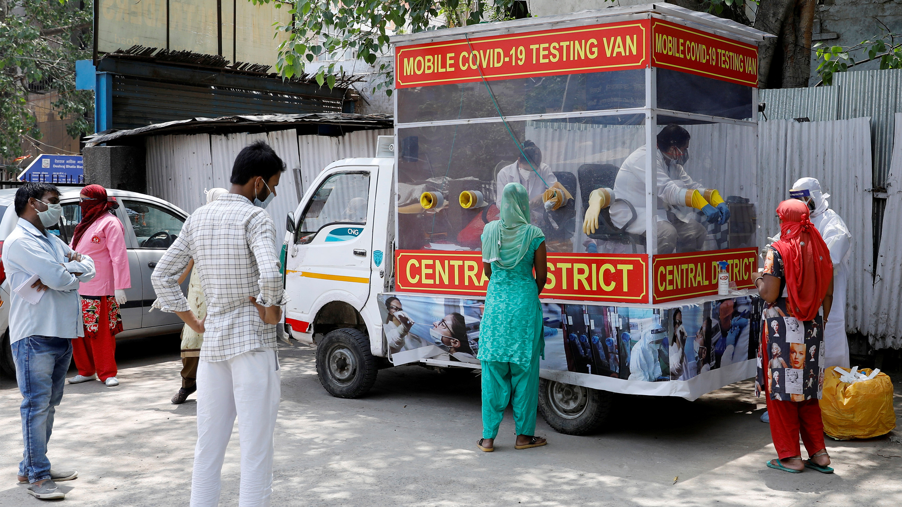 People in India stand near a red van that serves as a mobile testing center for COVID-19 .