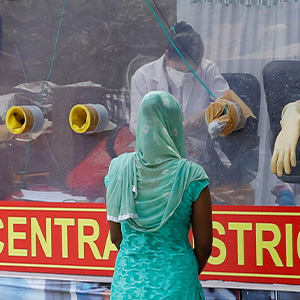 People in India stand near a red van that serves as a mobile testing center for COVID-19 .