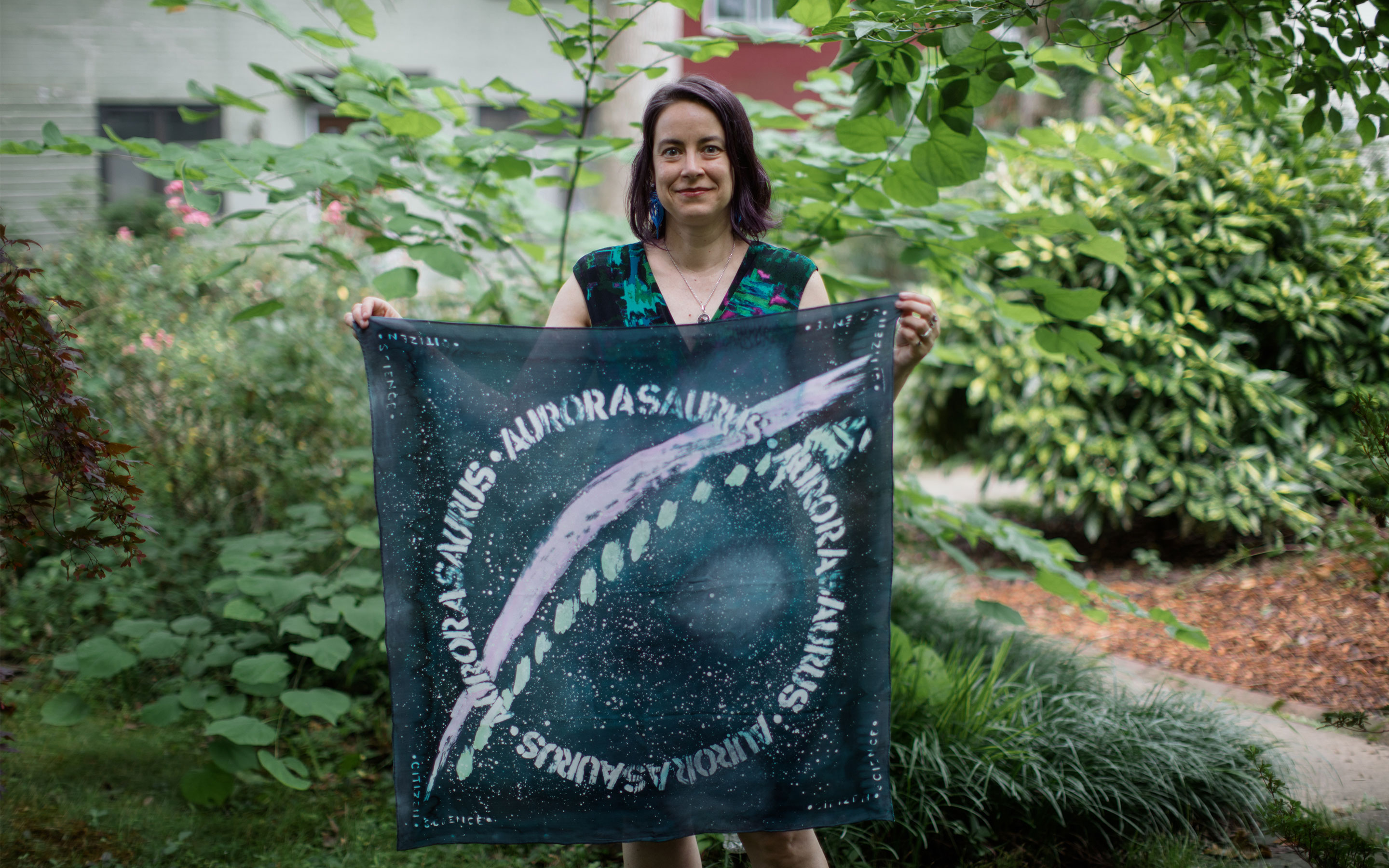 Liz MacDonald holding a banner printed with the STEVE aurora.