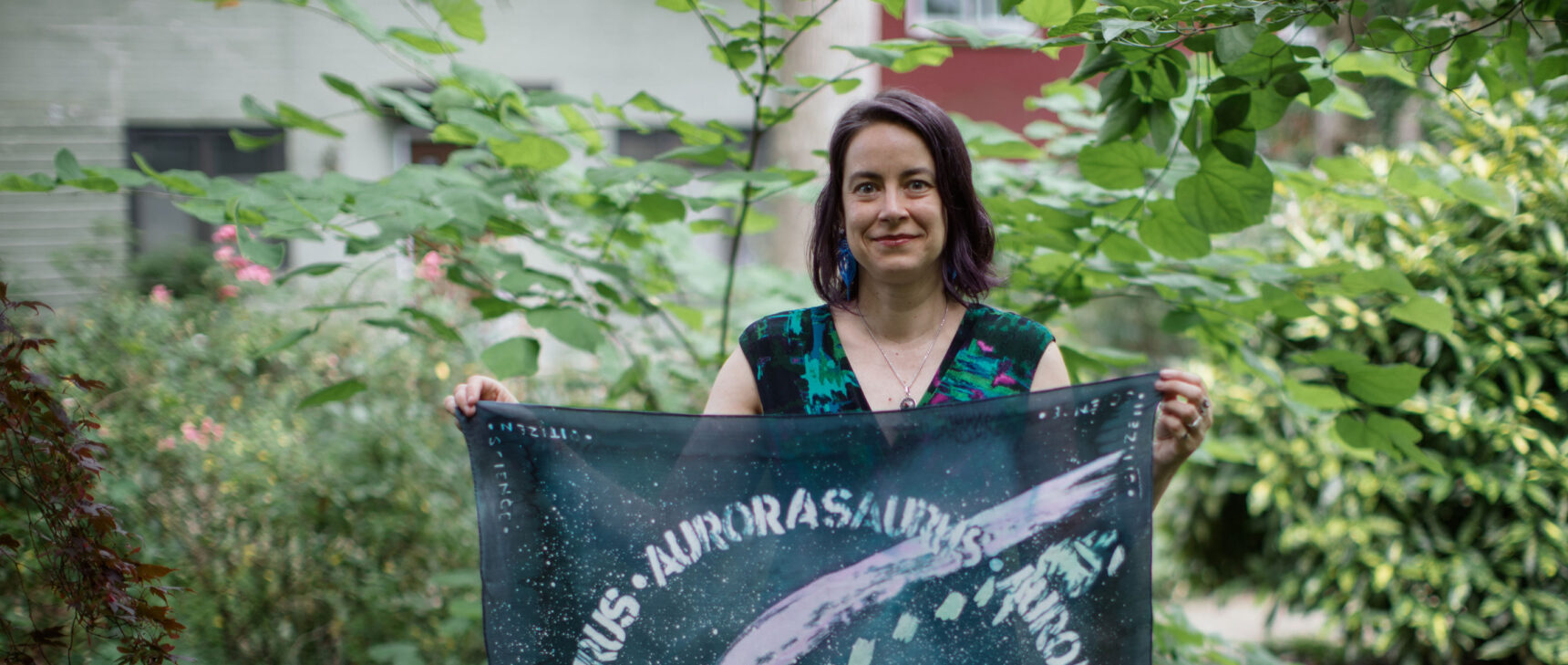 Liz MacDonald holding a banner printed with the STEVE aurora.