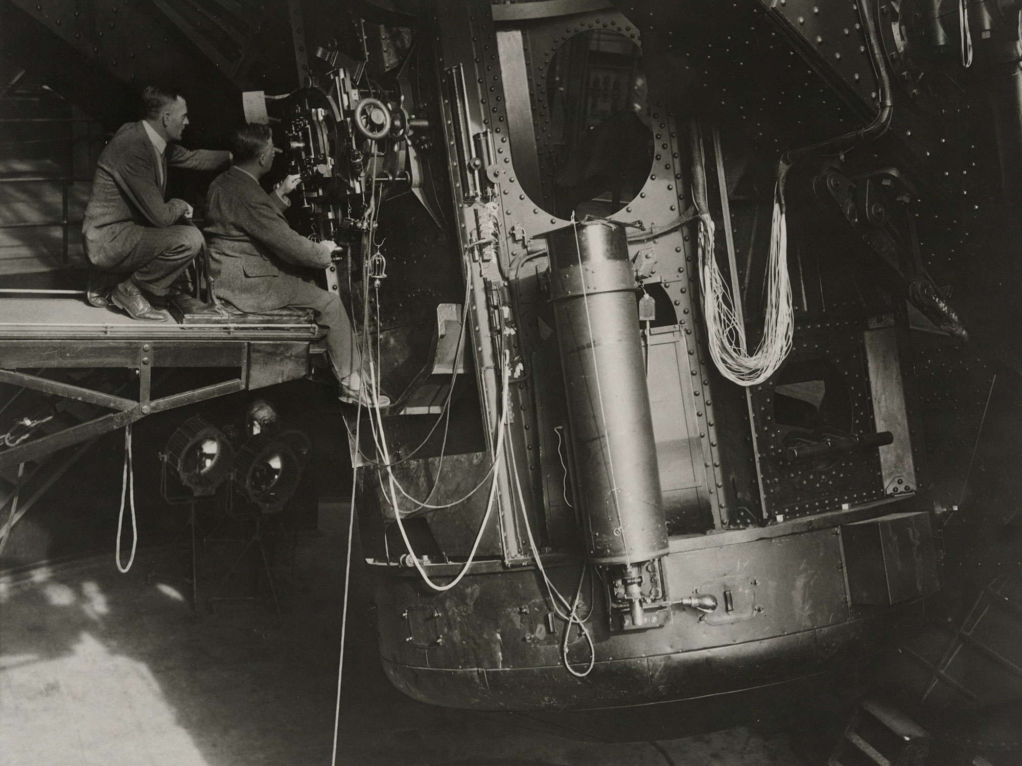 Black-and-white photo of Edwin Hubble and James Jeans at the eyepiece of a huge telescope.