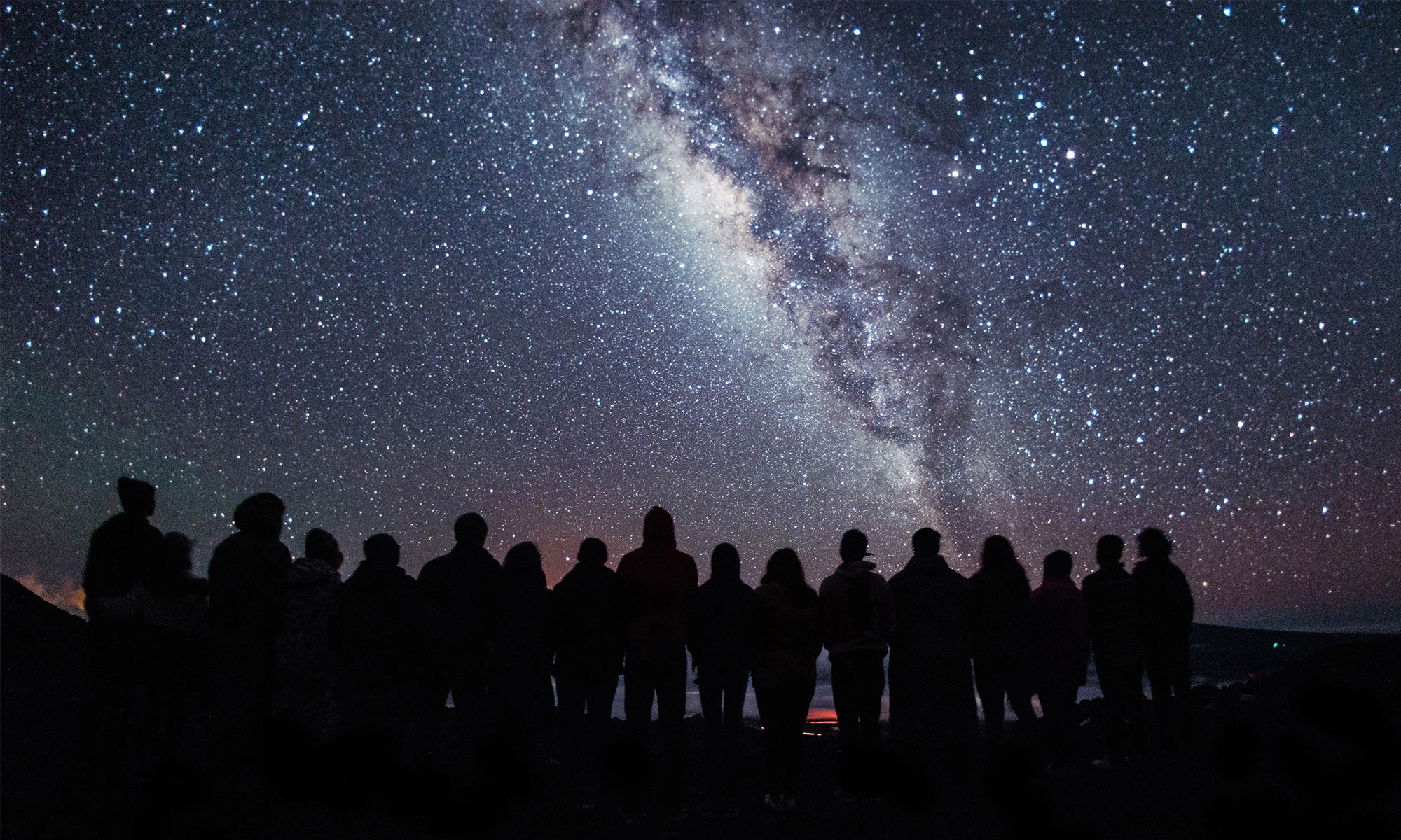 Photo of a group of people silhouetted against the Milky Way.