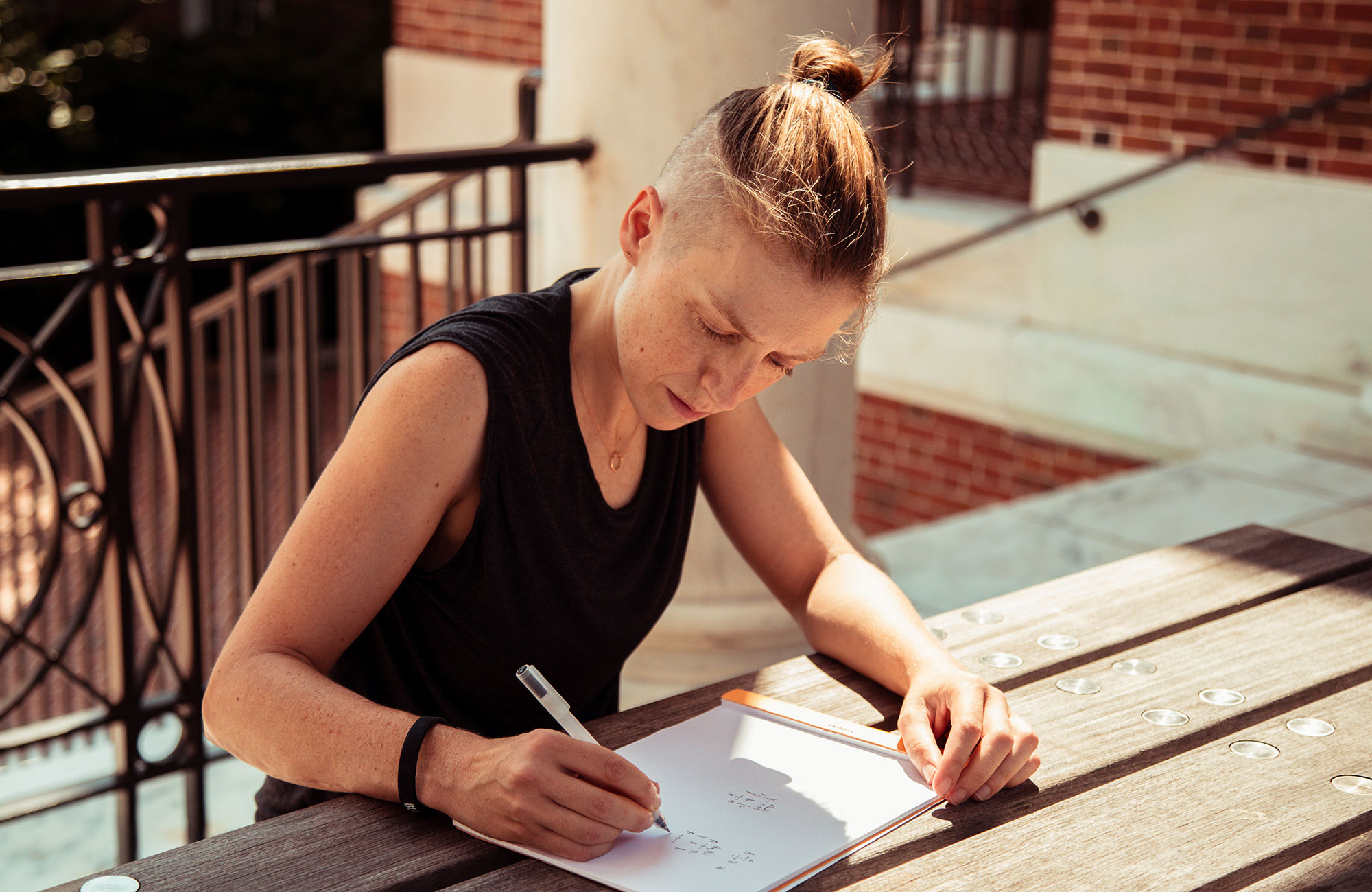 Riehl writing in a notebook at a table outside.