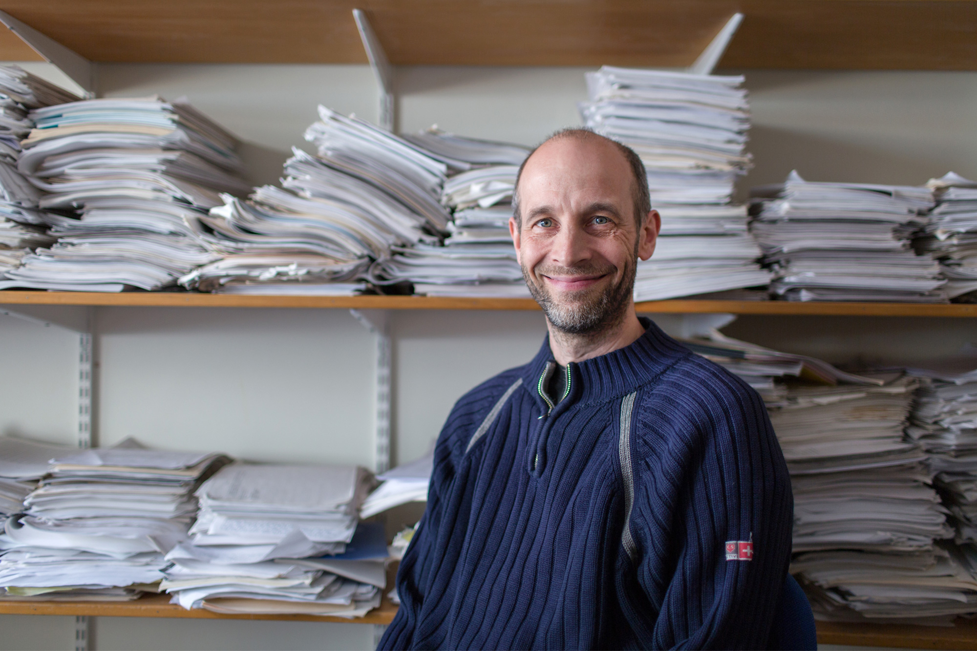 Portrait of Kevin Buzzard standing in front of stacks of papers