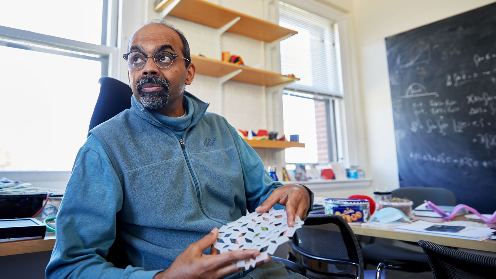 L. Mahadevan sits in his office, holding a white molded gel that resembles kirigami paper