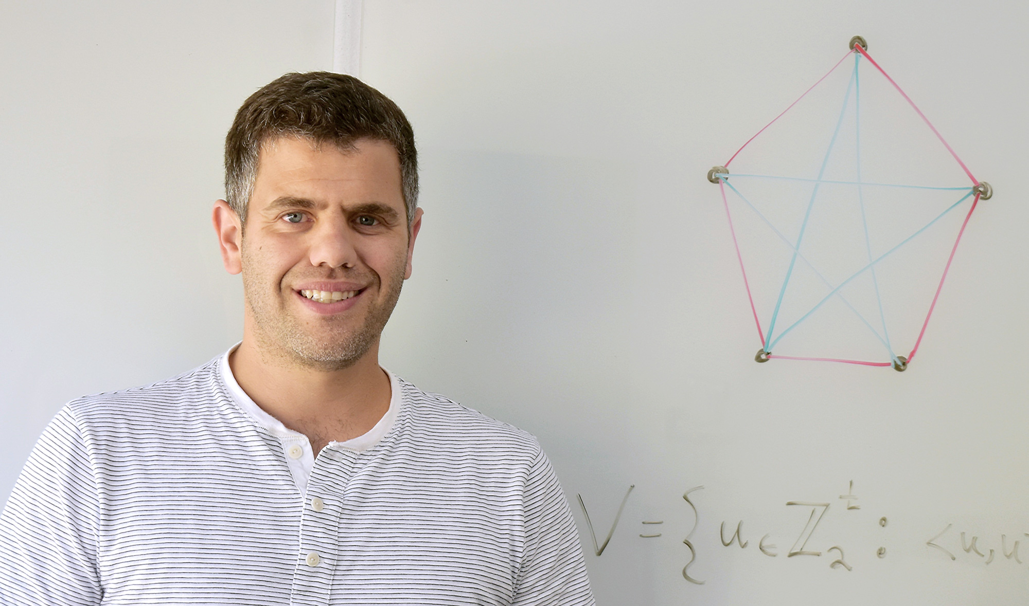 Photo of Asaf Ferber in front of a white board displaying a complete graph