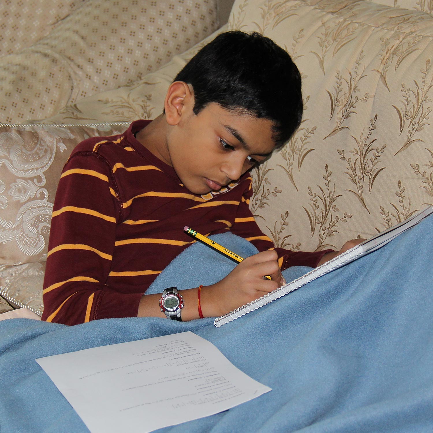 Photo of a young Ashwin Sah, working on math on a couch under a blue blanket