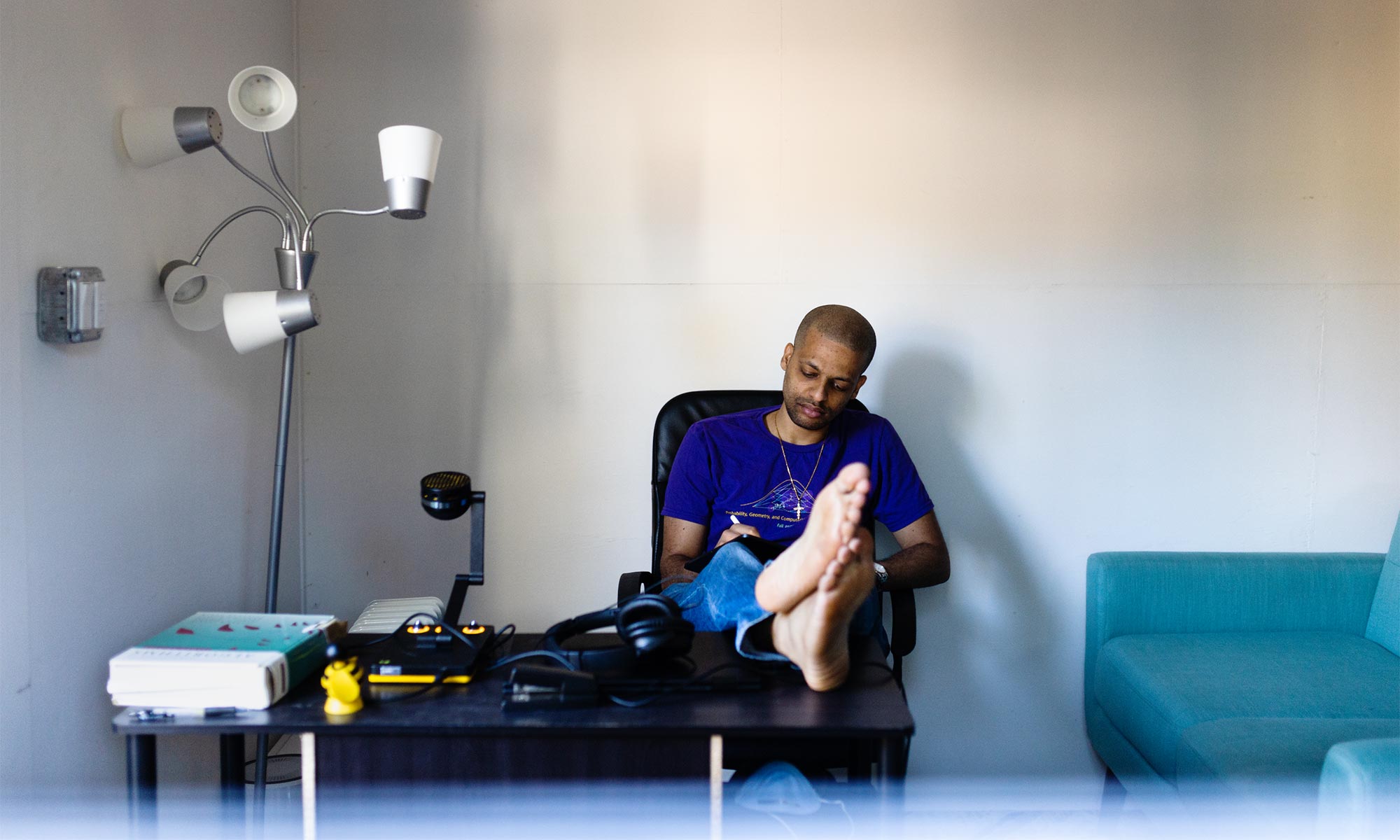 A diptych. Left image is Jelani Nelson sitting in a chair, writing in a notebook on his lap, with his feet up on his desk. Right image is of Nelson’s laptop screen showing code he is working on.