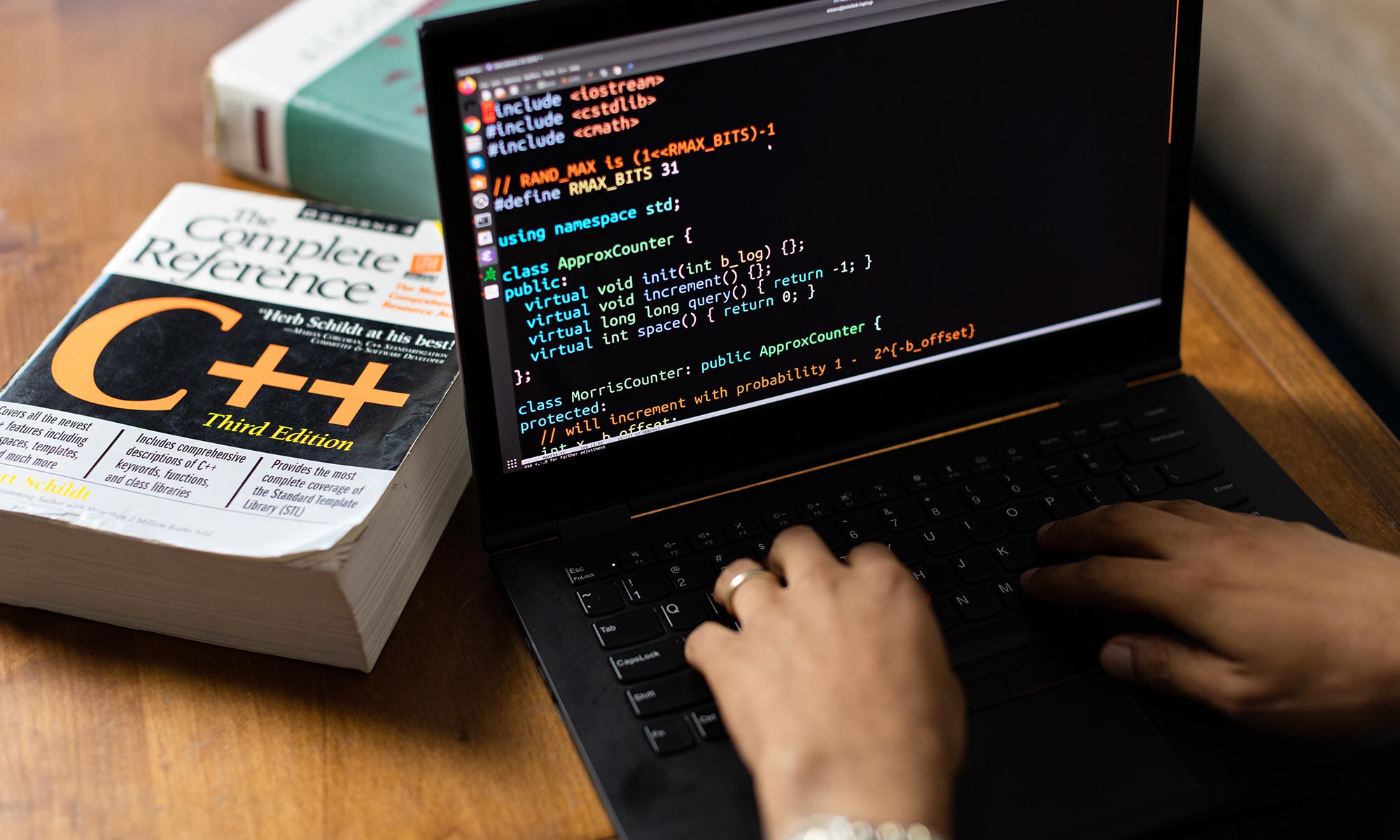 A diptych. Left image is Jelani Nelson sitting in a chair, writing in a notebook on his lap, with his feet up on his desk. Right image is of Nelson’s laptop screen showing code he is working on.