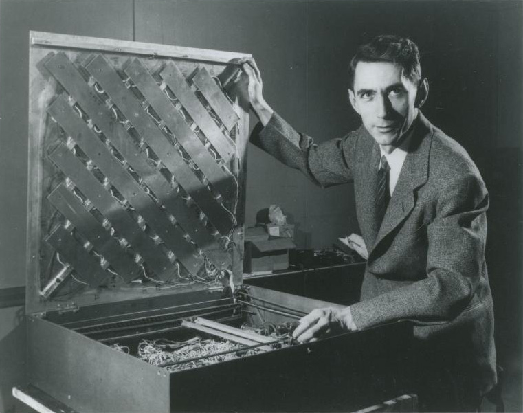 Black and white photo of Claude Shannon in front of a box filled with electronics