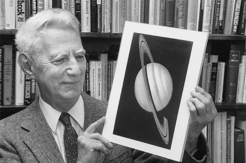 A black and white photo of an older Claude Shannon looking at a photo of Saturn