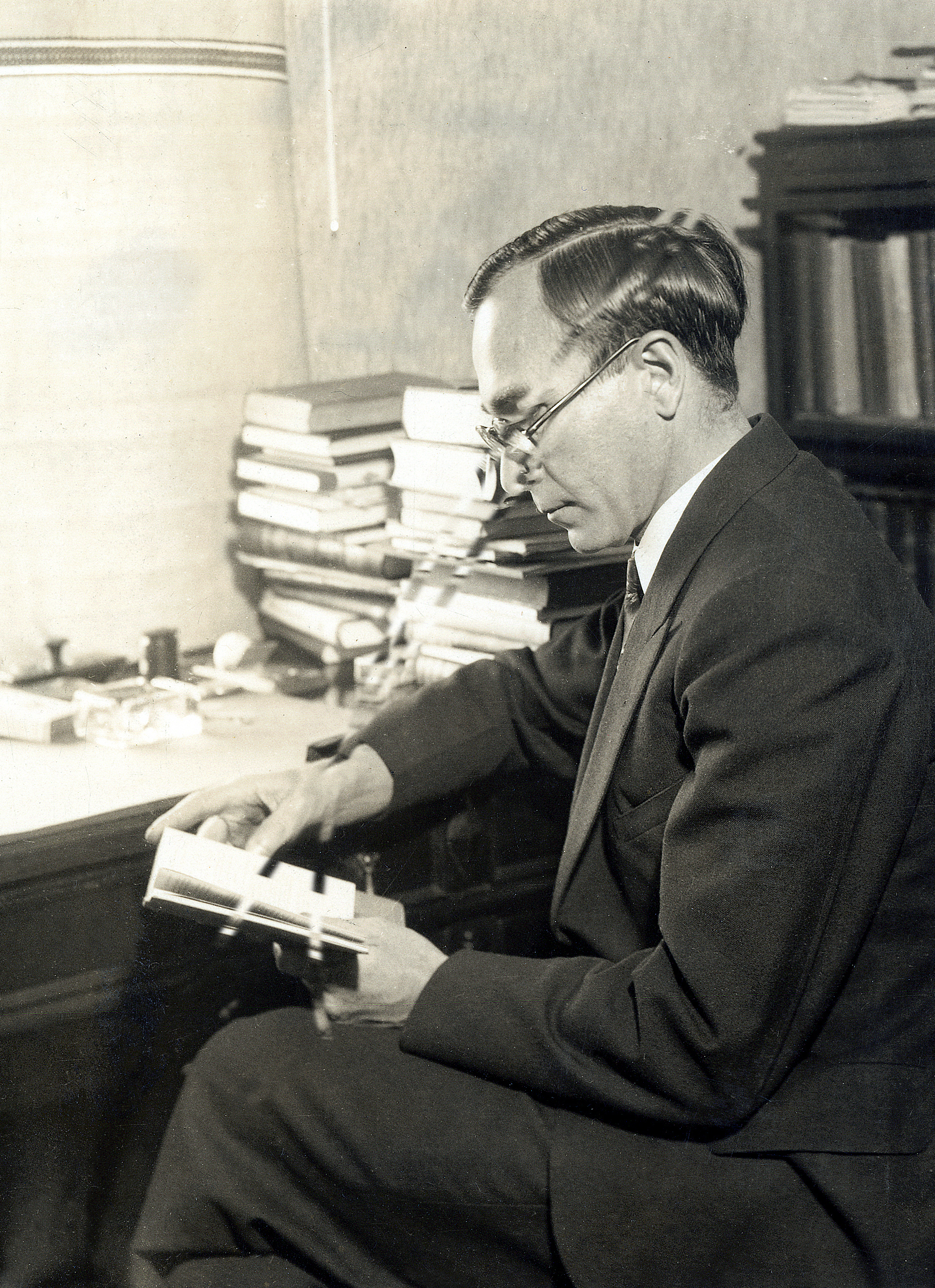 Black-and-white photo of Tibor Radó wearing a suit and glasses, sitting at a desk and reading a book.