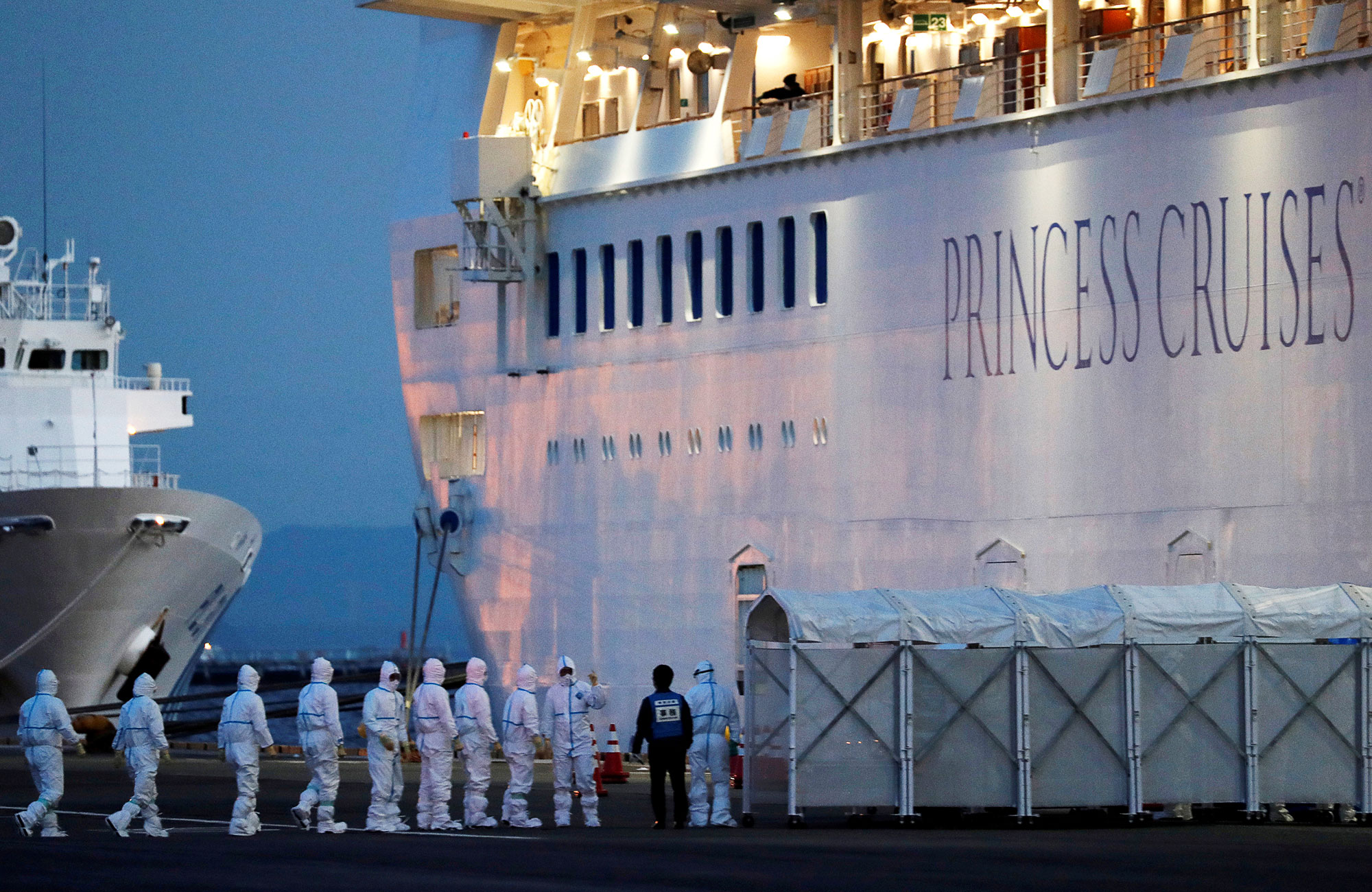 The Diamond Princess cruise ship in port, being boarded by a line of people in full protective gear.