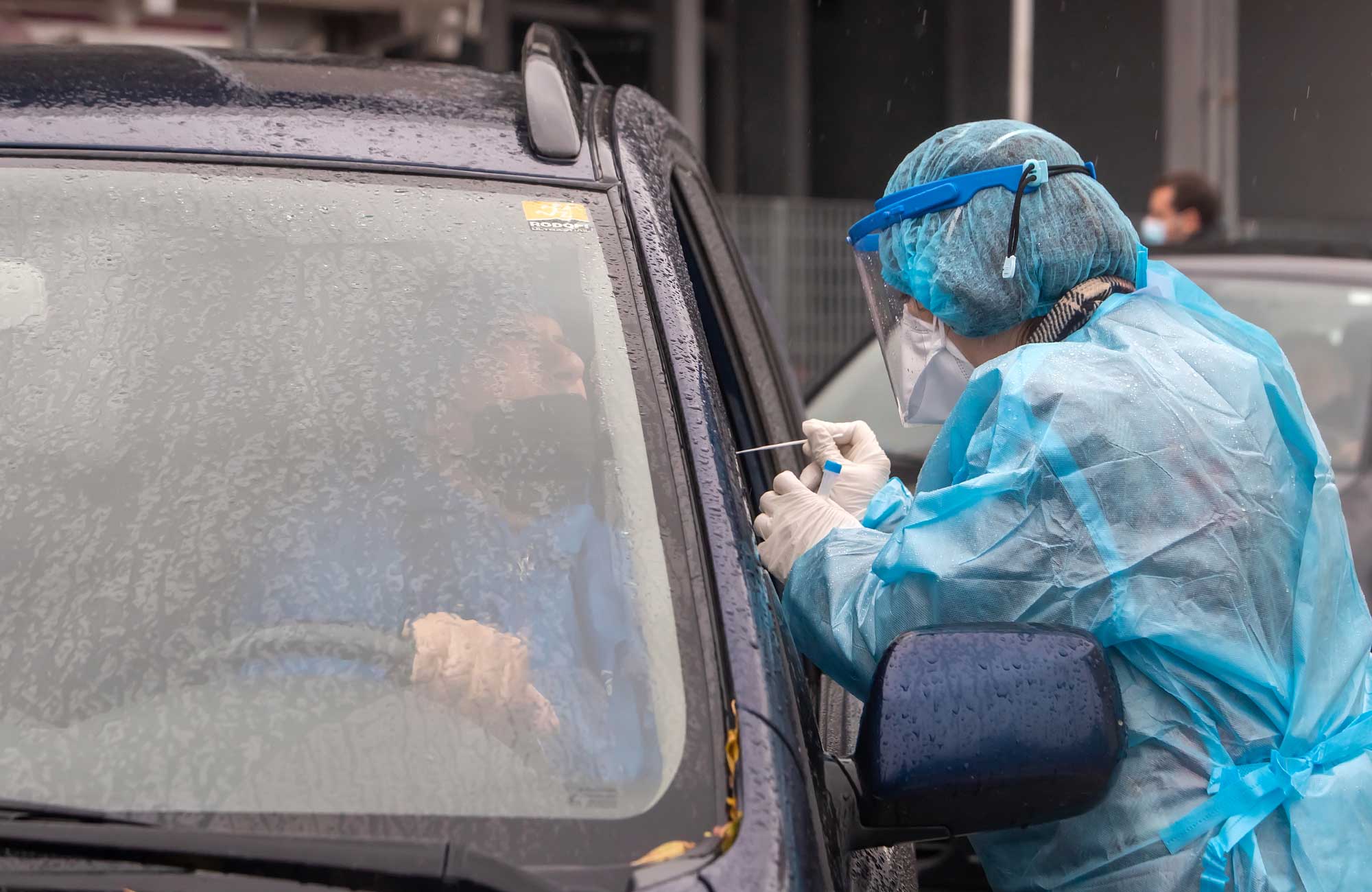 Healthcare worker in in full protective gear swab-tests a driver for COVID-19 exposure.