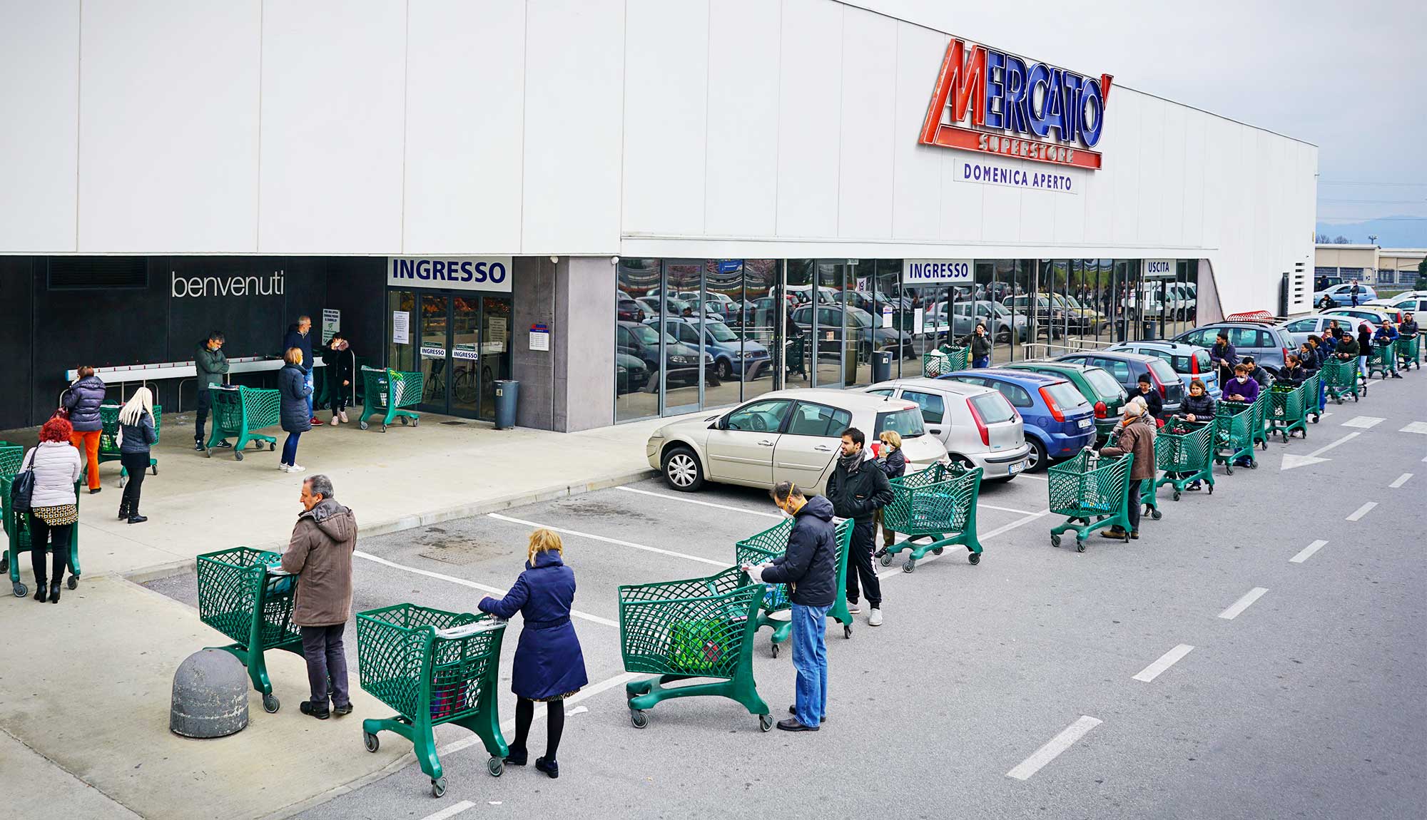 Shoppers with carts wait in a socially distanced line outside a store in Milan.