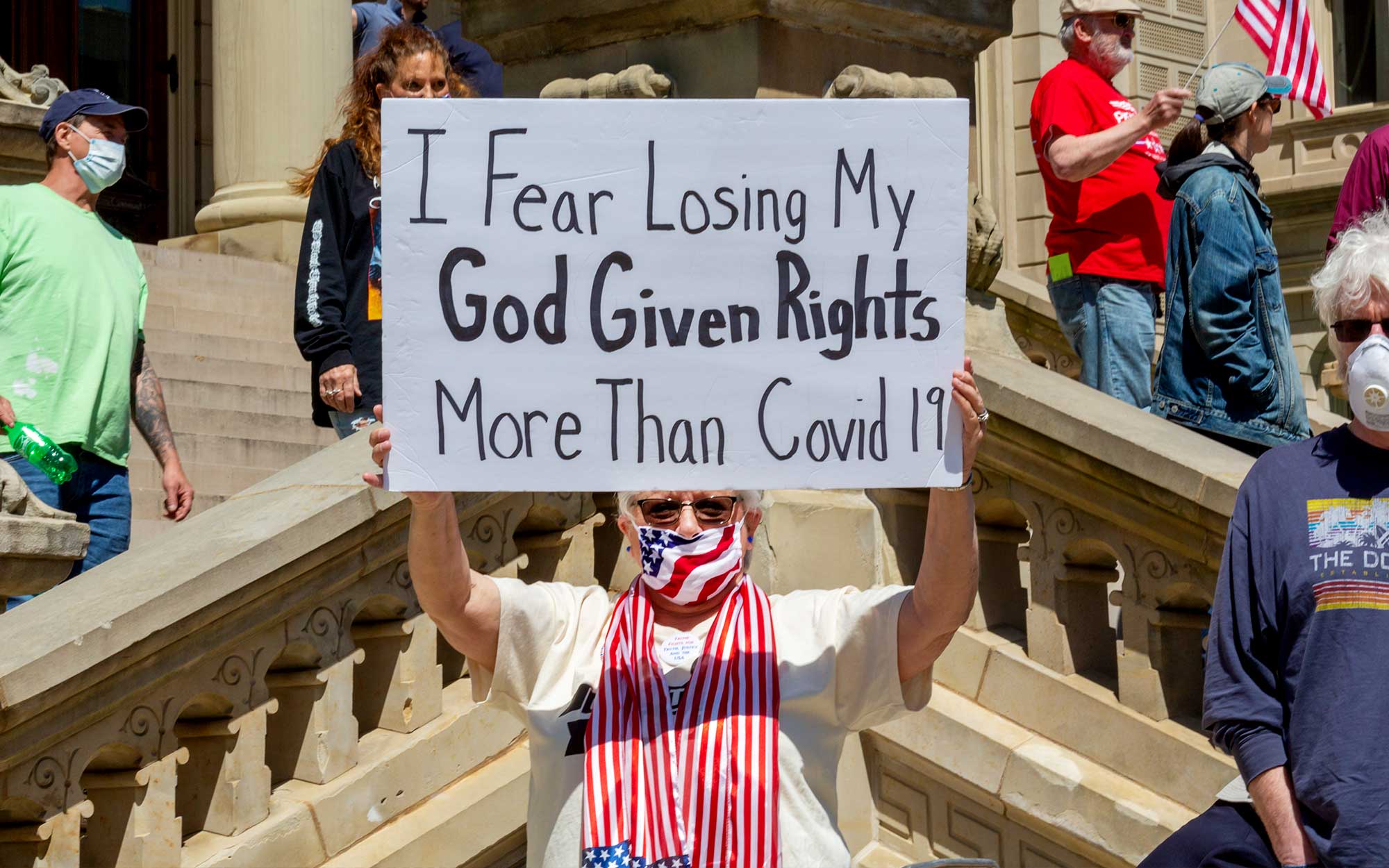 Photo of protestors, including one holding a sign at center that says, “I fear losing my God given rights more than Covid-19.”