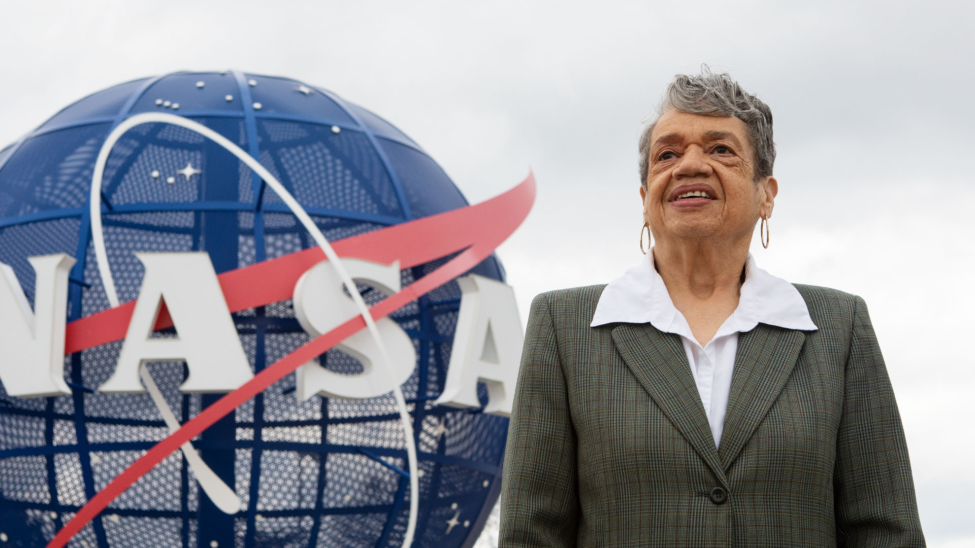 Photo of Christine Darden in front of a statue of the NASA "meatball" logo at NASA Langley