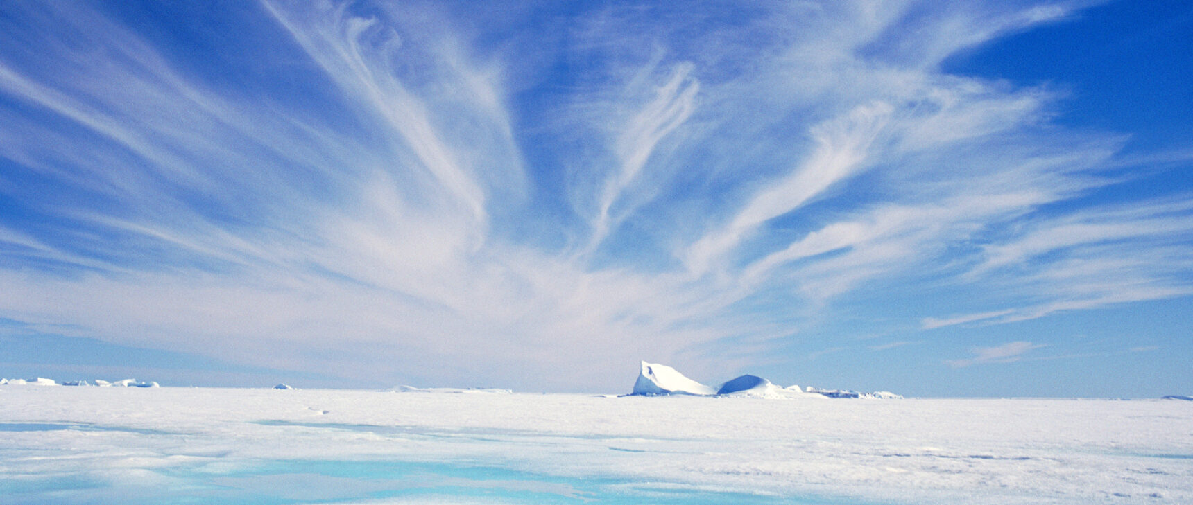 Photograph showing cirrus clouds in a blue sky above an expanse of flat, snow-covered ice.