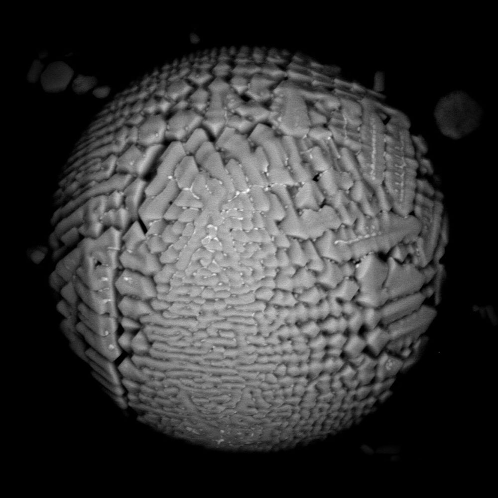 Black-and-white image of a spherical cosmic dust grain with a corrugated surface.