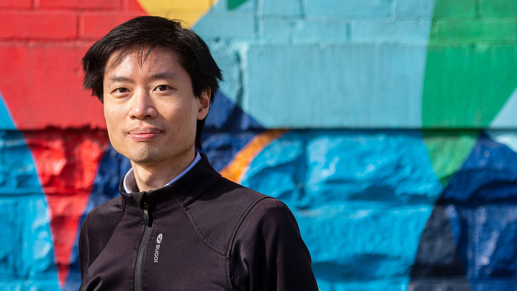 Po-Shen Loh standing on a stairway in front of a colored wall outside of his office in Pittsburgh.