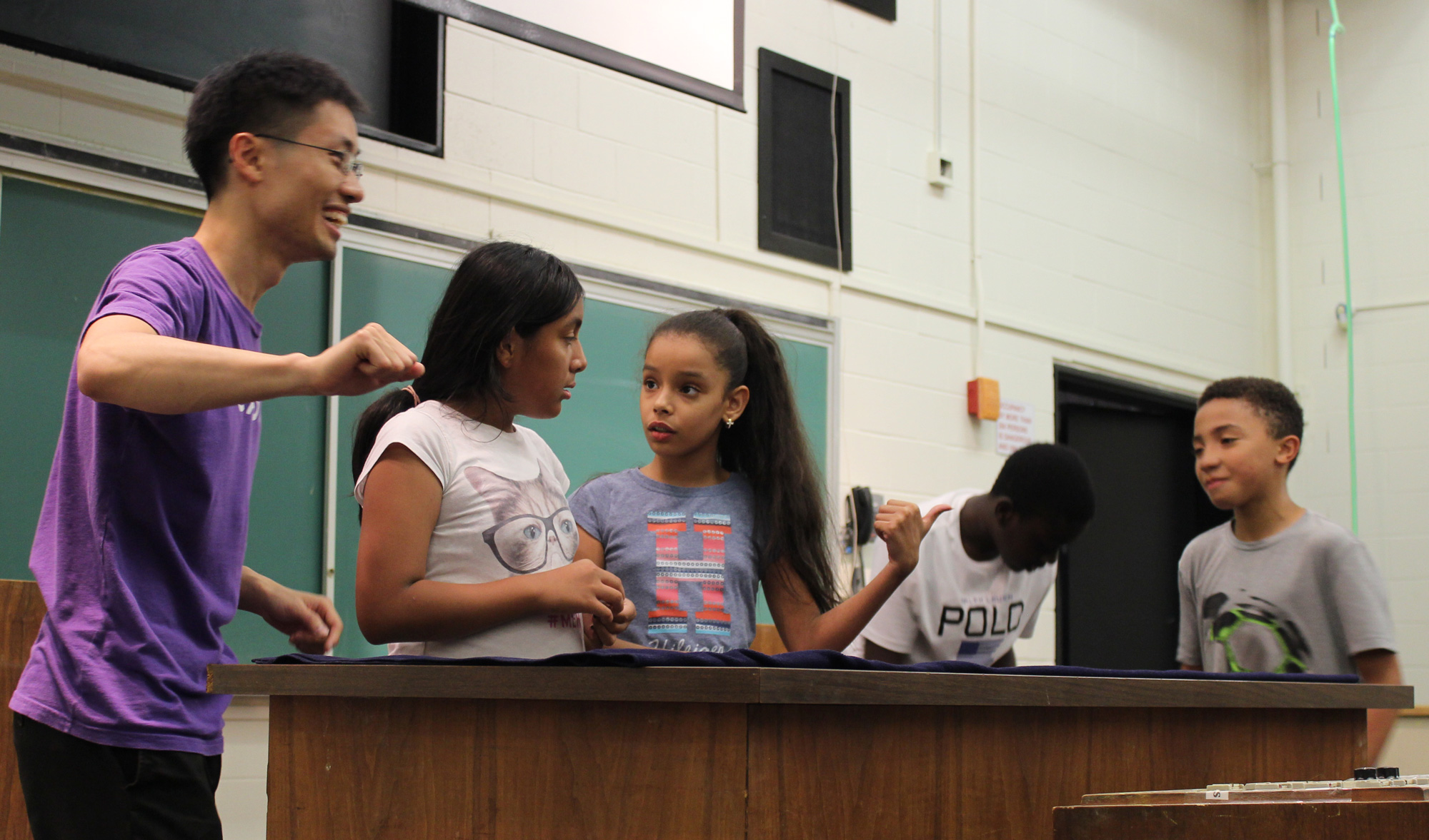 Loh standing in a classroom and giving a guest lecture with four young students standing near him.