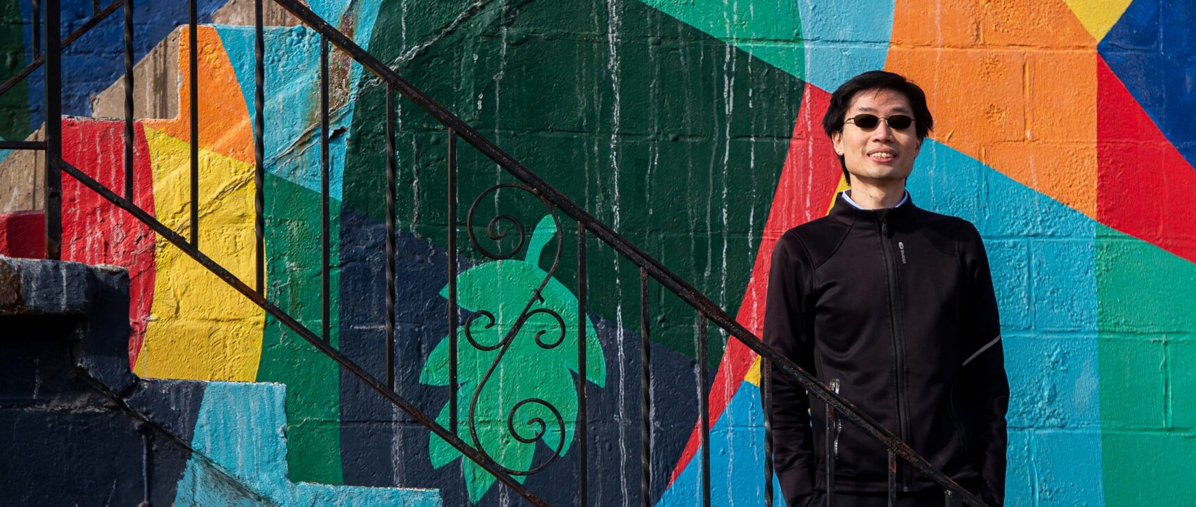 Po-Shen Loh standing on a stairway in front of a colored wall outside of his office in Pittsburgh.