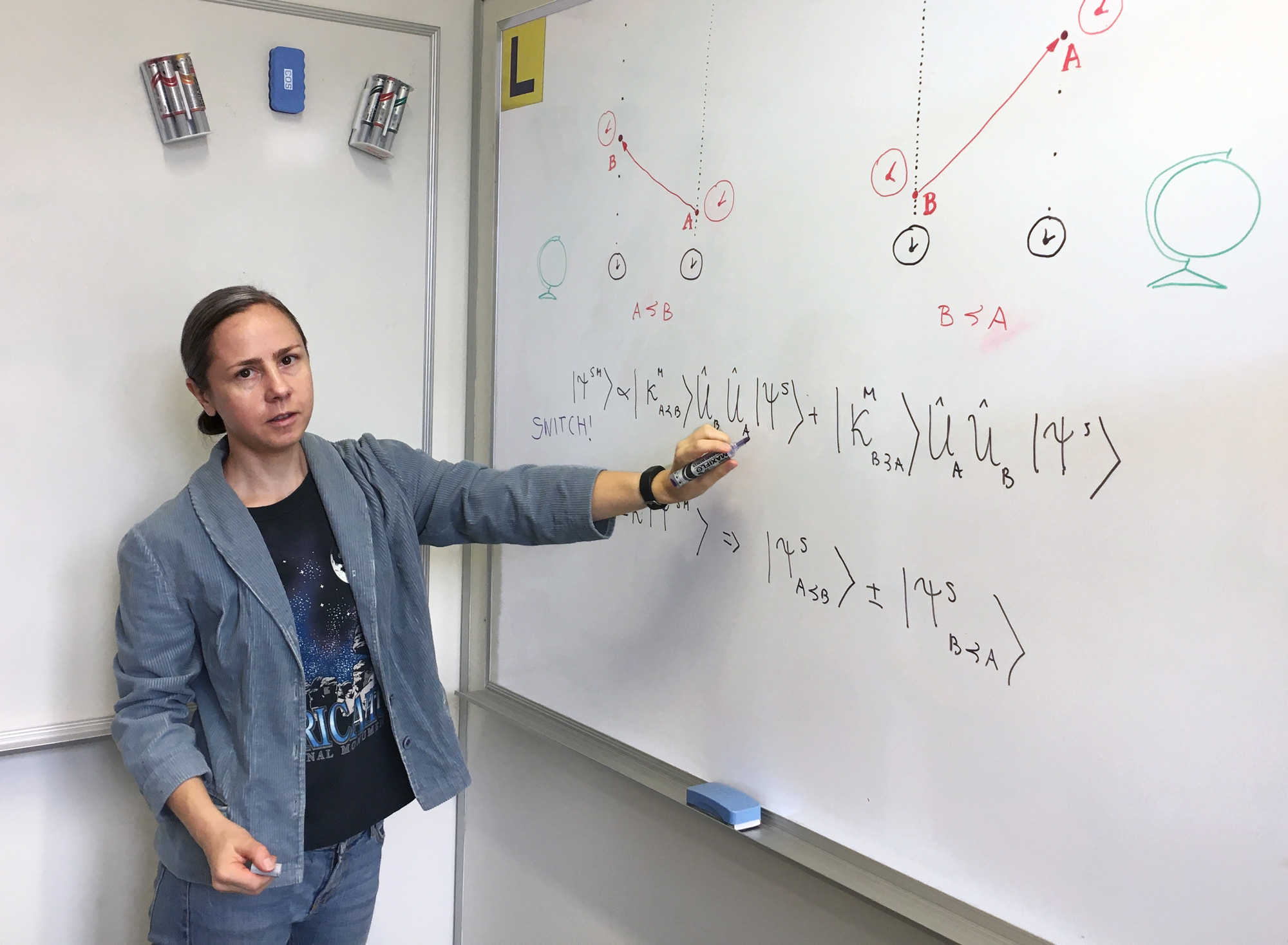 A diptych of two photos; one shows a bald man in glasses with arms crossed leaning against a blackboard and the other shows a woman in a blazer using a marker to point at an equation on a whiteboard.